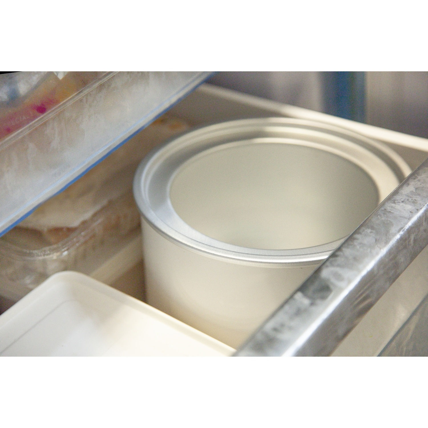 Een witte container met zilveren rand staat in een lade naast andere containers.