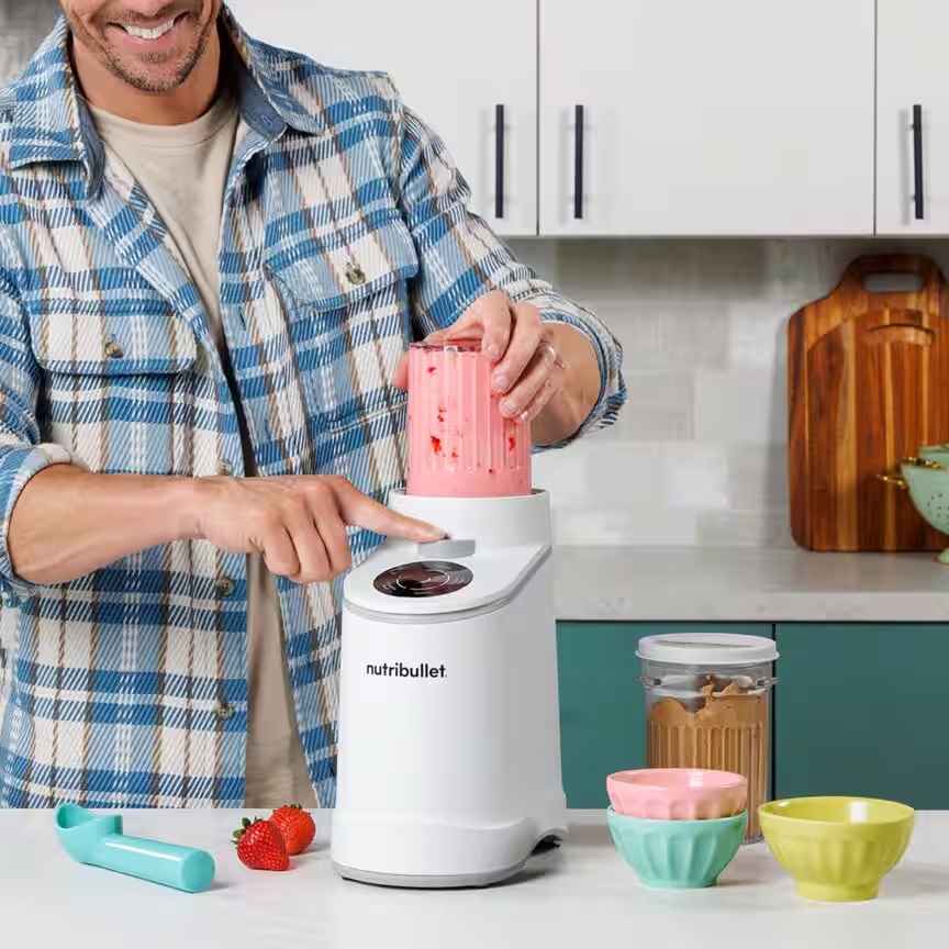 Férfi rózsaszín turmixot készít fehér Nutribulletban, eperrel és tálakkal.