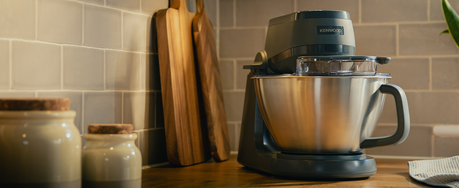 Szürke Kenwood konyhai robotgép rozsdamentes acél tálal, fa pulton.