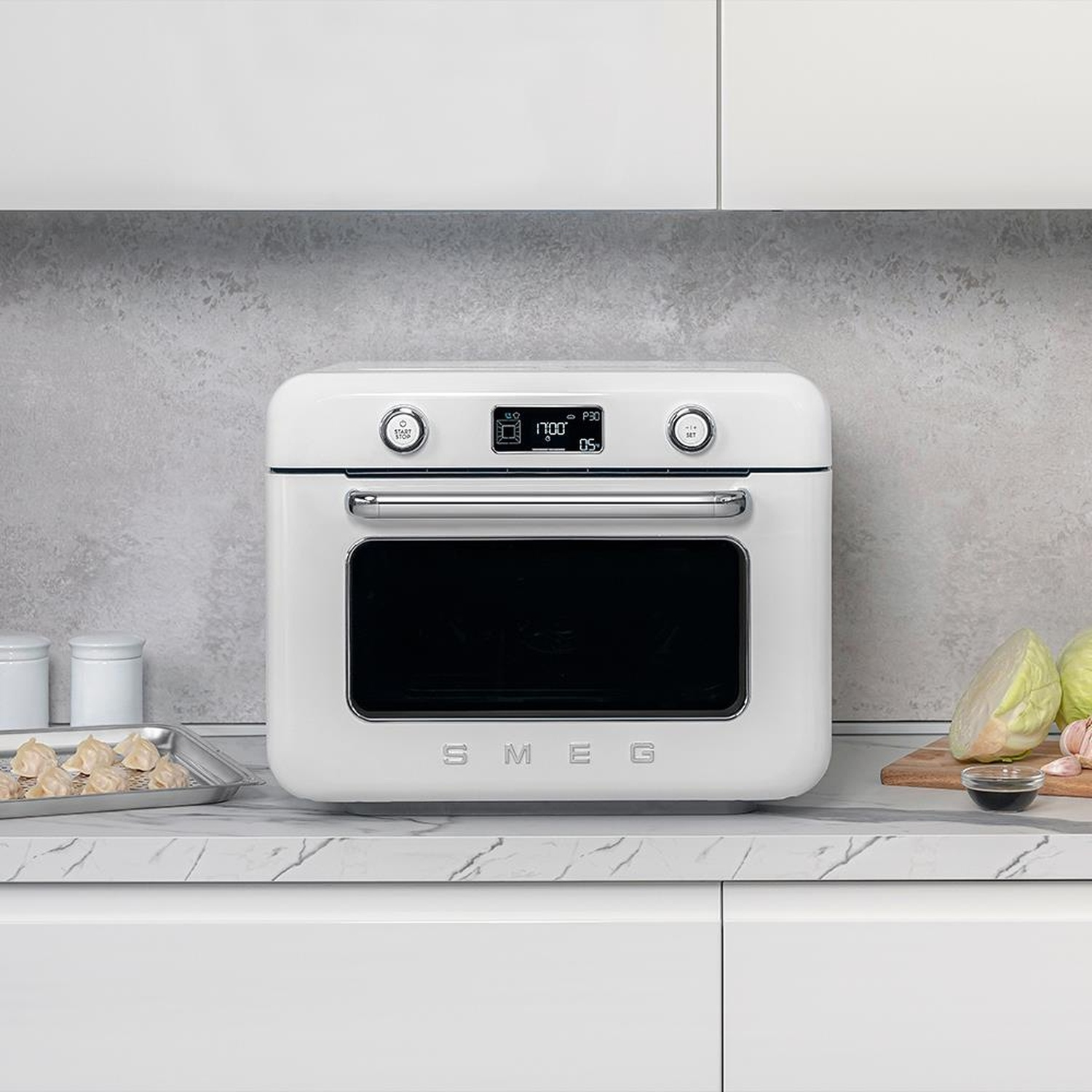 Un forno SMEG bianco su un piano di lavoro in marmo con ravioli e cavolo.