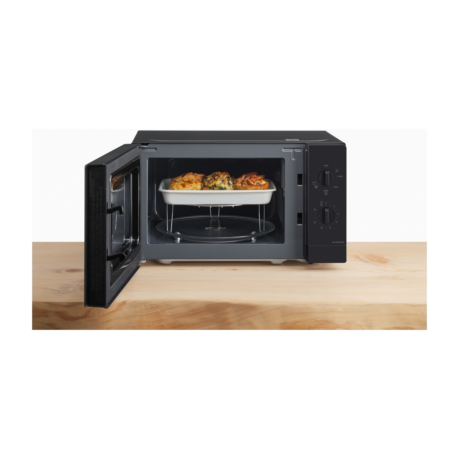 Forno a microonde nero con porta aperta, mostra un piatto bianco con cibo cotto su una griglia.