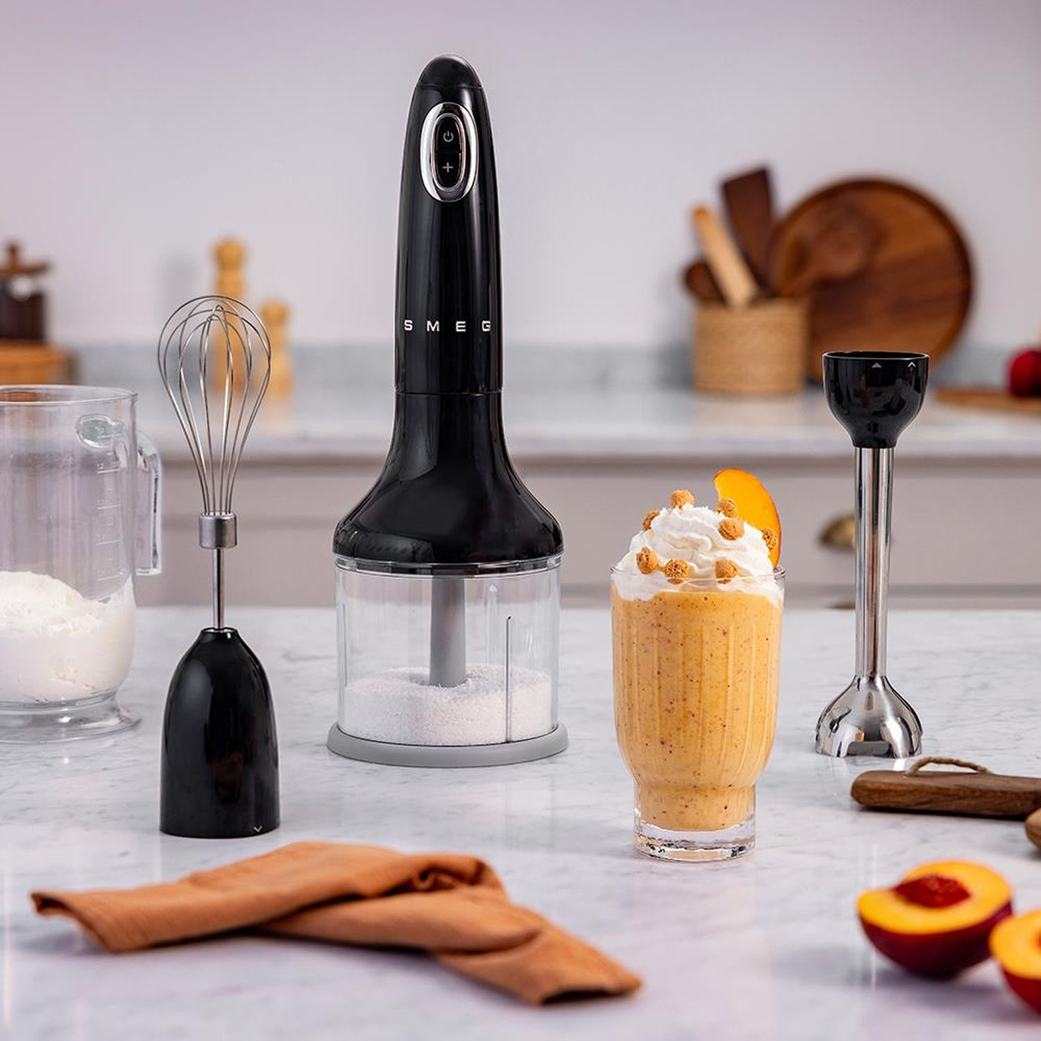Un frullatore a immersione nero con frusta, contenitore e un frullato di pesche.