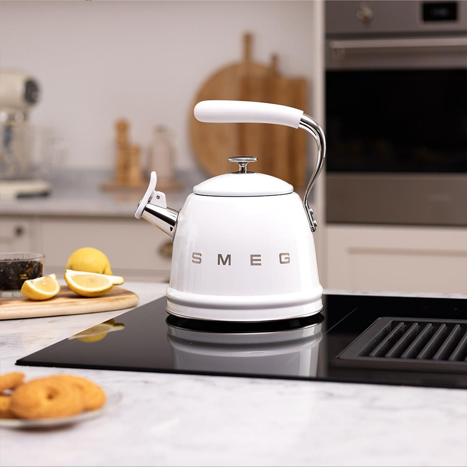 Un bollitore bianco Smeg su piano cottura a induzione con limoni e biscotti.