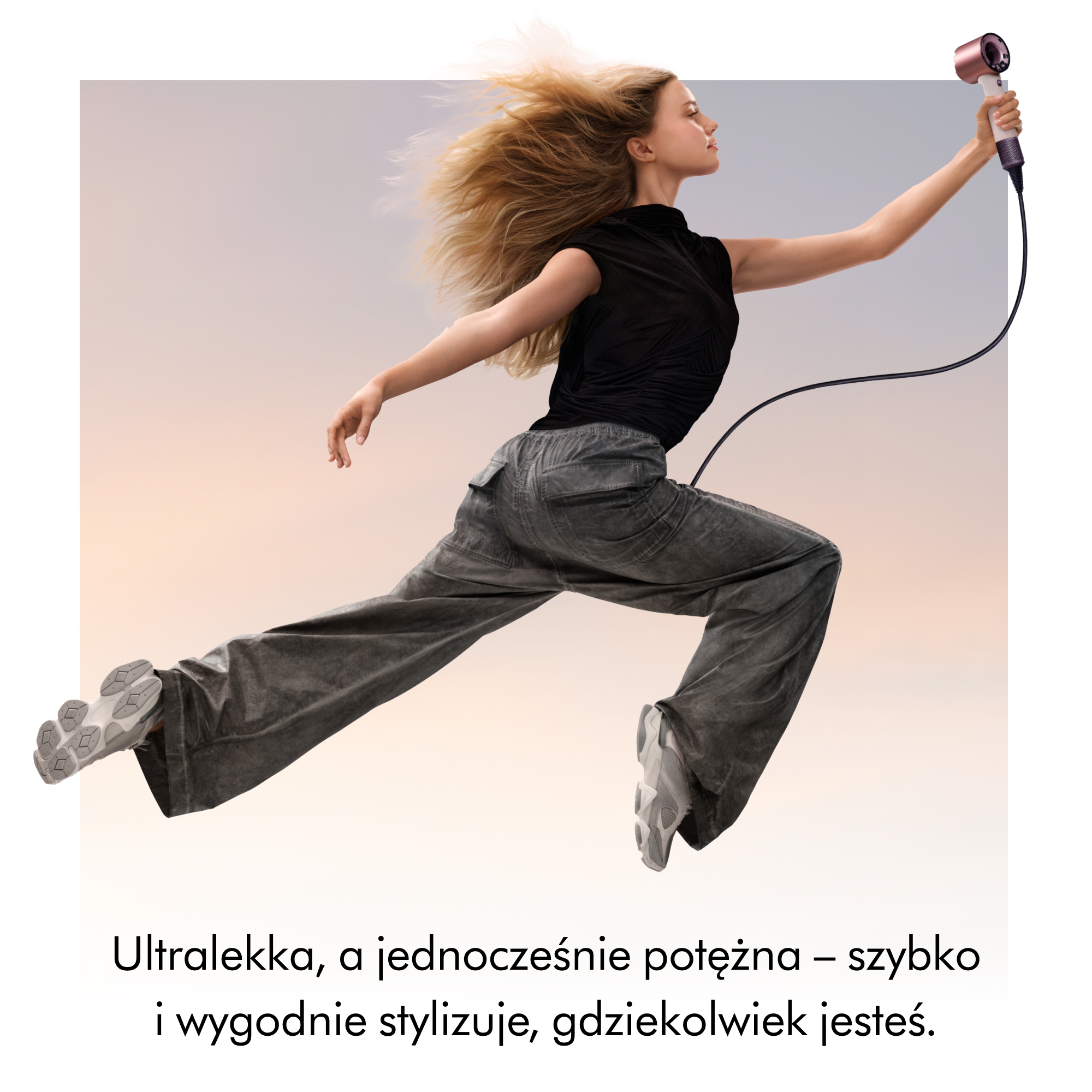 Kobieta z rozwianymi blond włosami trzyma w powietrzu suszarkę do włosów.