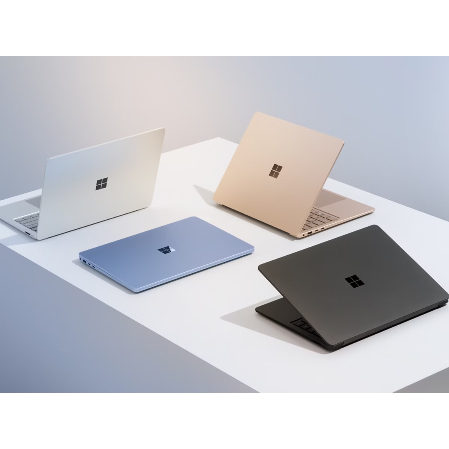 Three laptops in silver, gold, and black colors placed on a white surface.