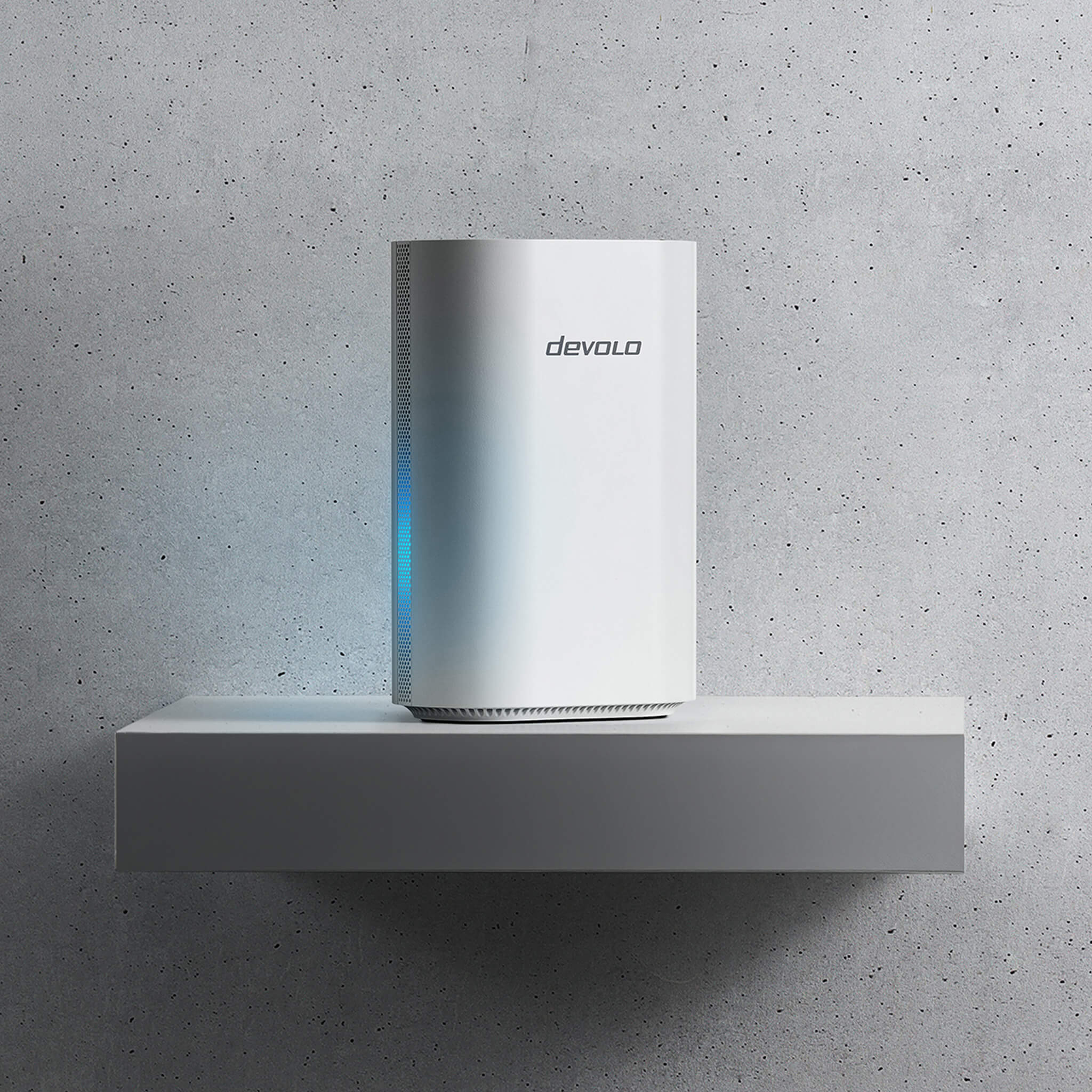 Ein weißer Devolo Router steht auf einem grauen Regal vor einer Betonwand.