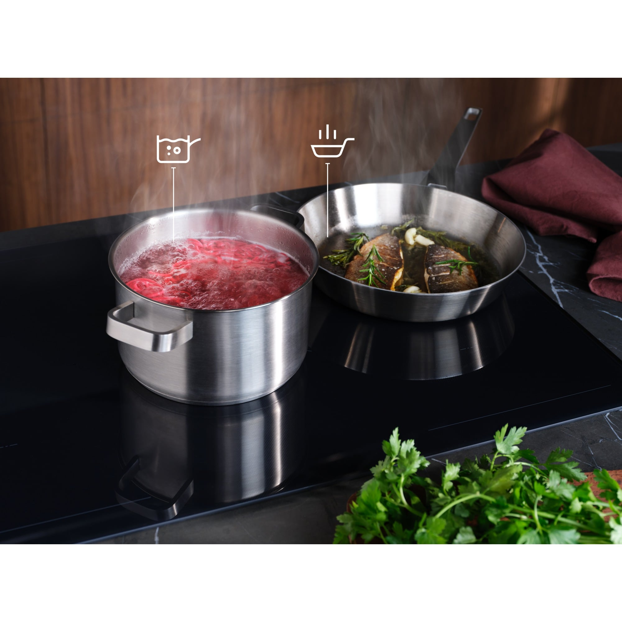 Una olla de comida roja hirviendo y una sartén con pescado en una placa de inducción.