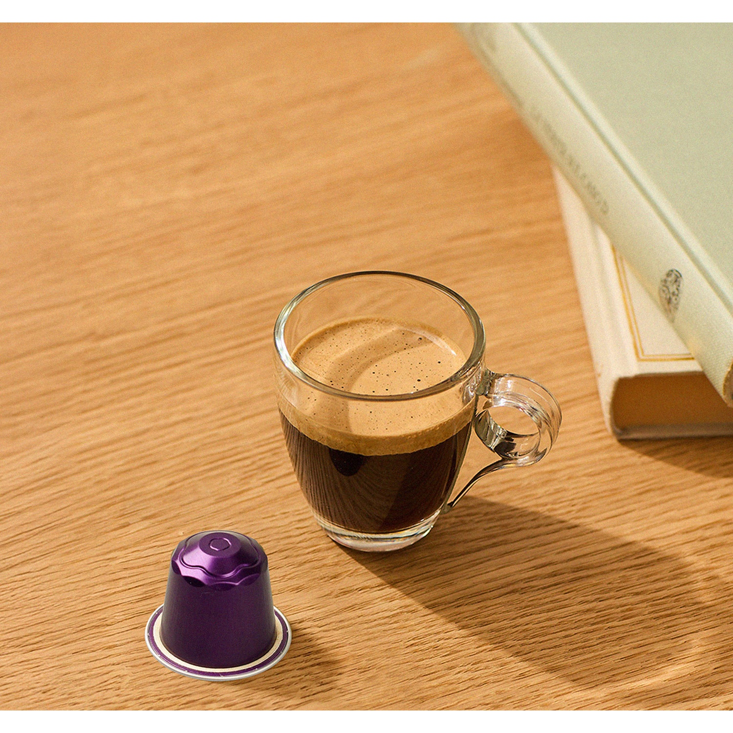 Un bicchiere di espresso con crema e una capsula viola su un tavolo di legno.