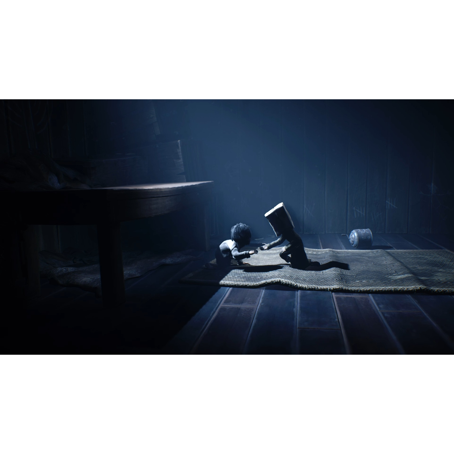 A small child crawls on a rug in a dark room next to a table.