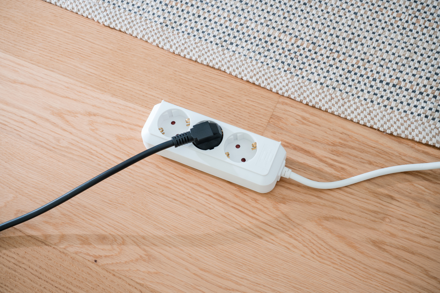 Ein weier Mehrfachsteckdosenverteiler mit einem schwarzen Stecker auf Holzboden.