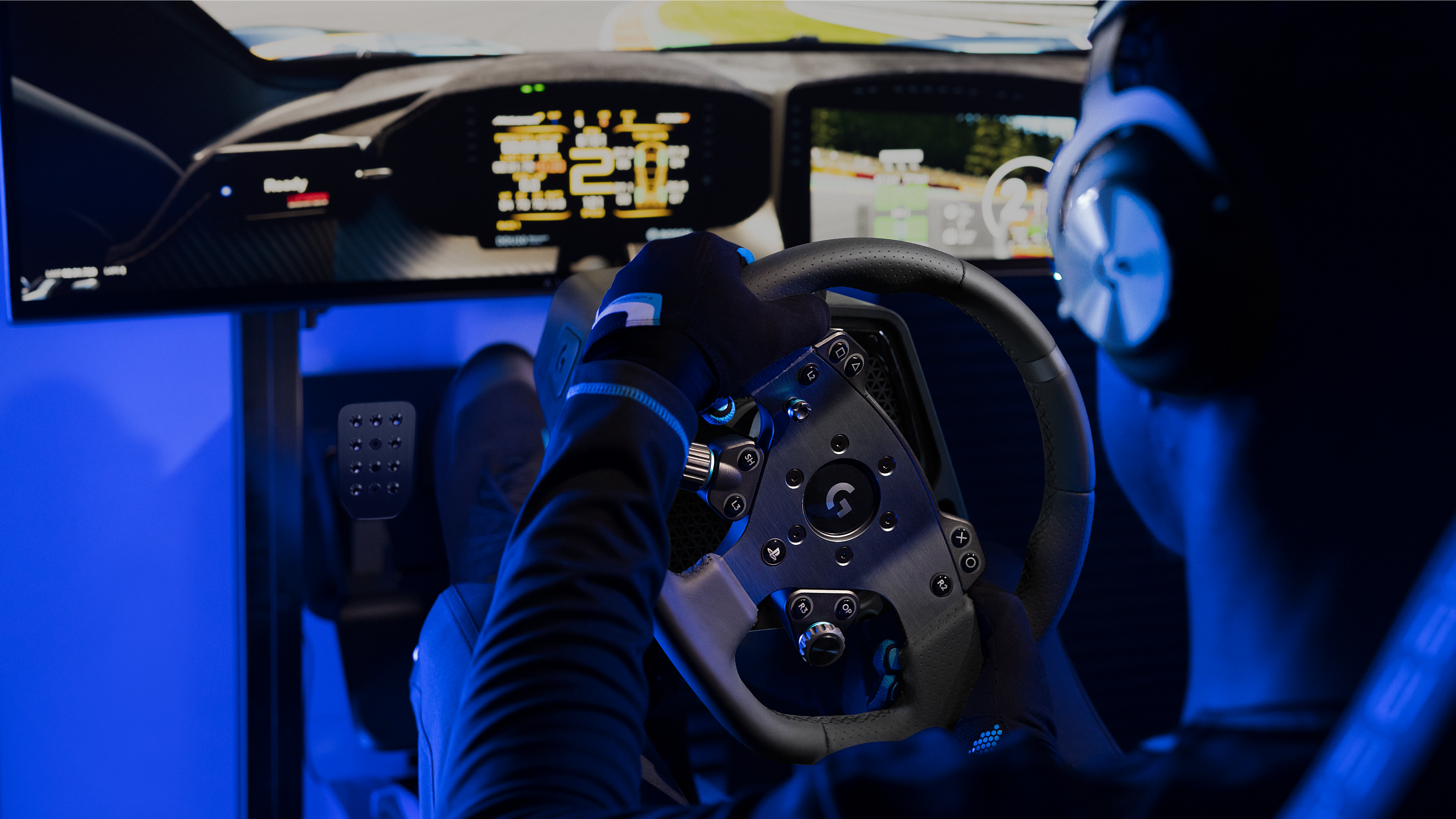 Personne portant des gants et un casque joue à un jeu de course sur simulateur avec écran et pédales.