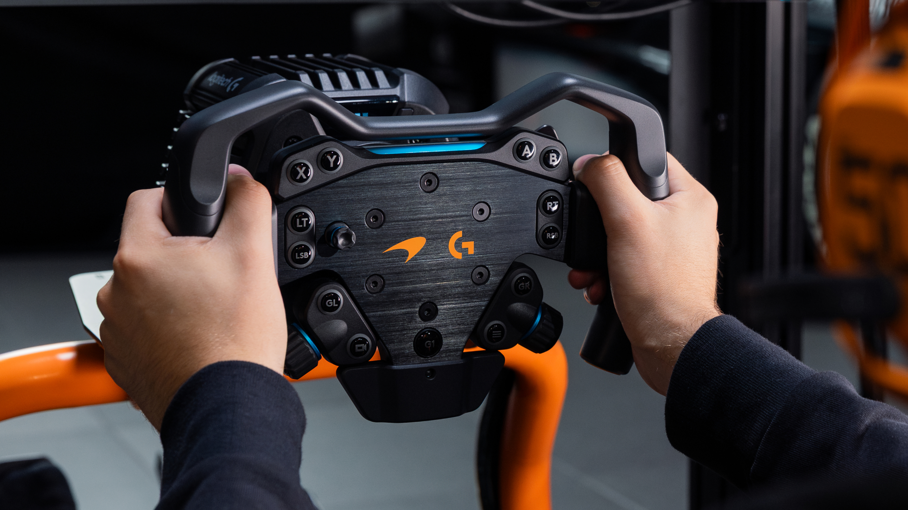 Mains tenant un volant Logitech G noir avec des accents orange.