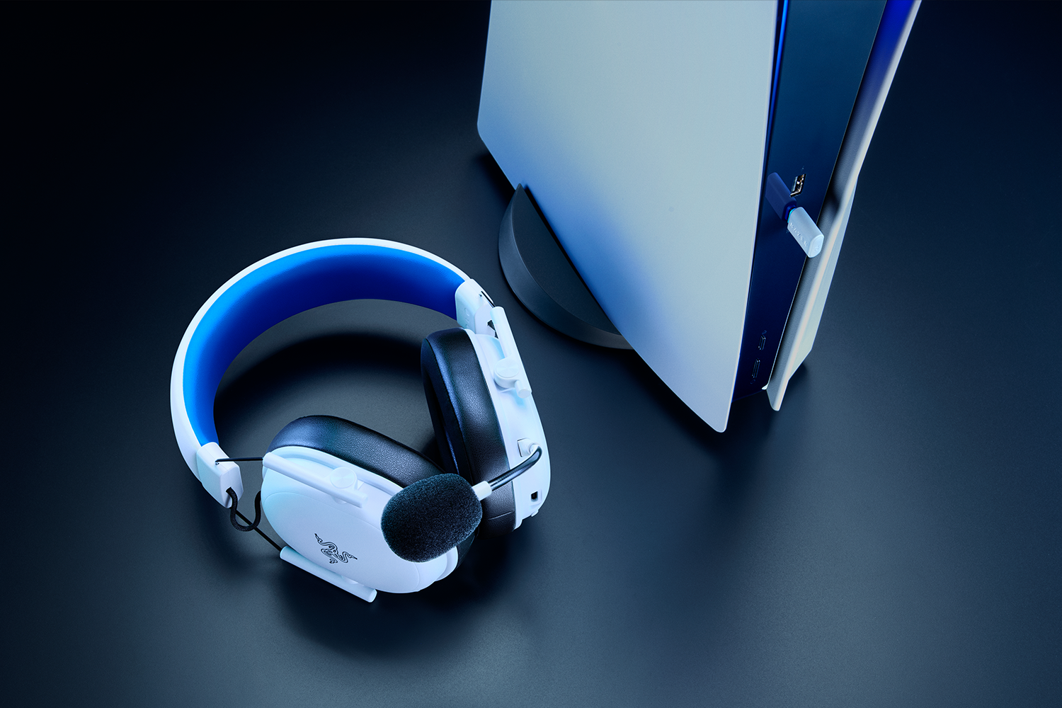Weiß-blaues Gaming-Headset mit Mikrofon auf dunklem Untergrund, neben einer weißen Spielkonsole.