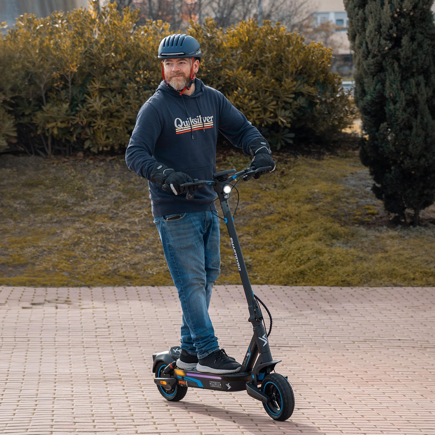Un hombre con casco monta un patinete eléctrico negro por un camino pavimentado.