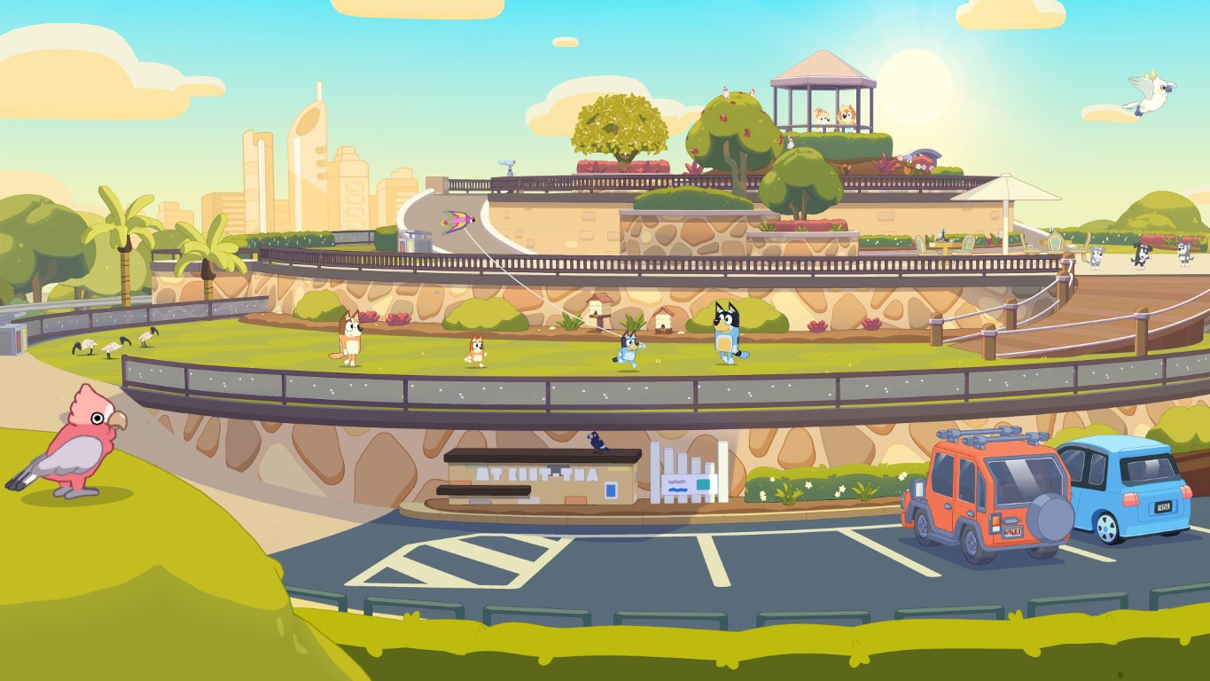 Różowa papuga galah stoi na zielonej trawie. Psy i miasto w tle.