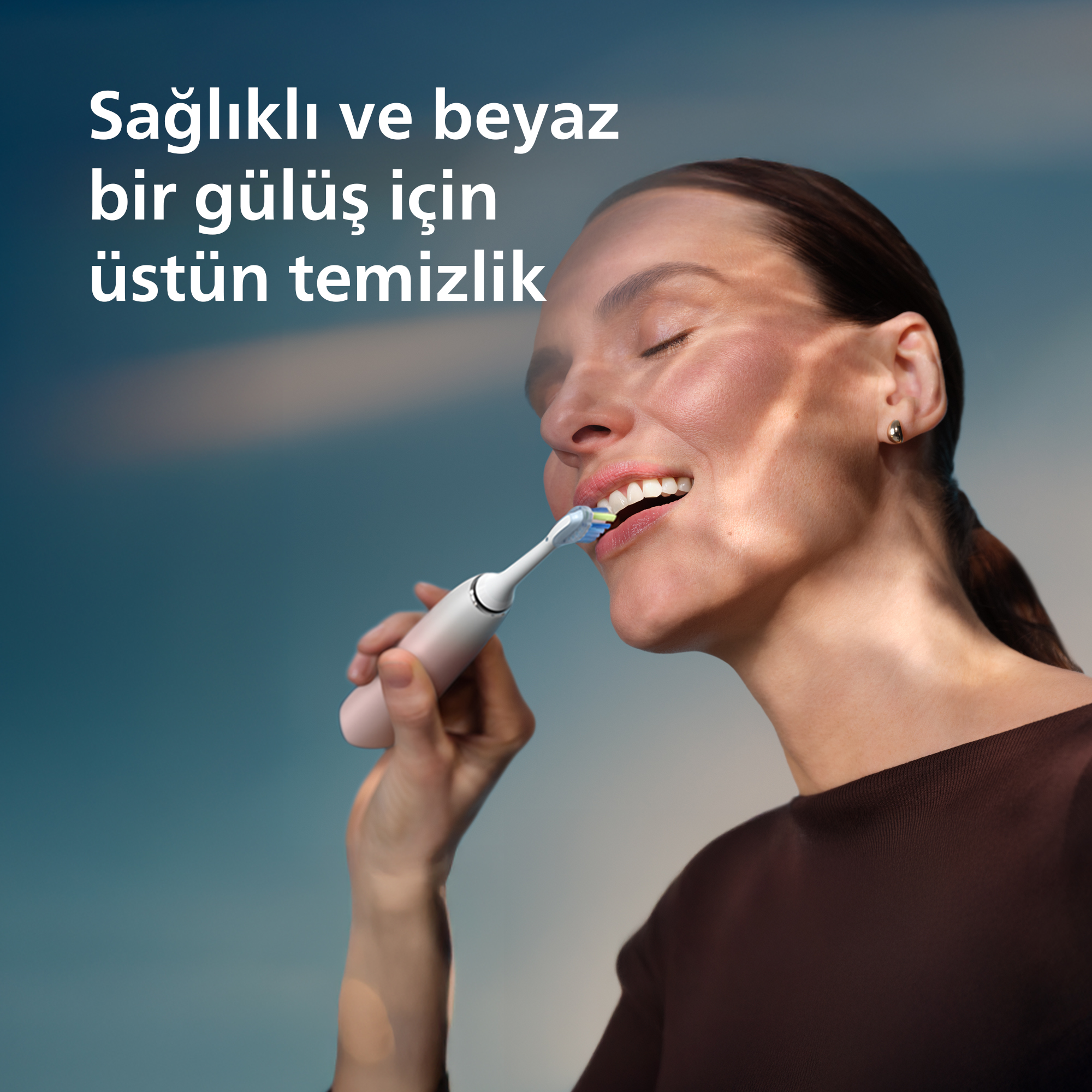Bir kadın elektrikli diş fırçasıyla dişlerini fırçalıyor.