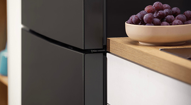 Miska czerwonych winogron na drewnianej powierzchni obok czarnych szafek kuchennych.