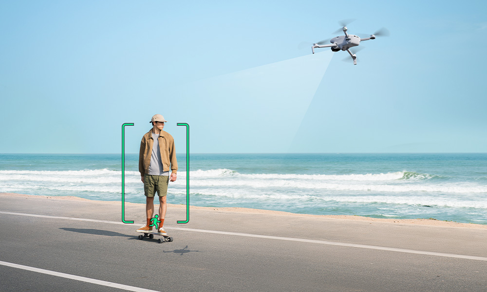 Dron filmuje mężczyznę na deskorolce przy plaży. Jasne niebo, ocean.