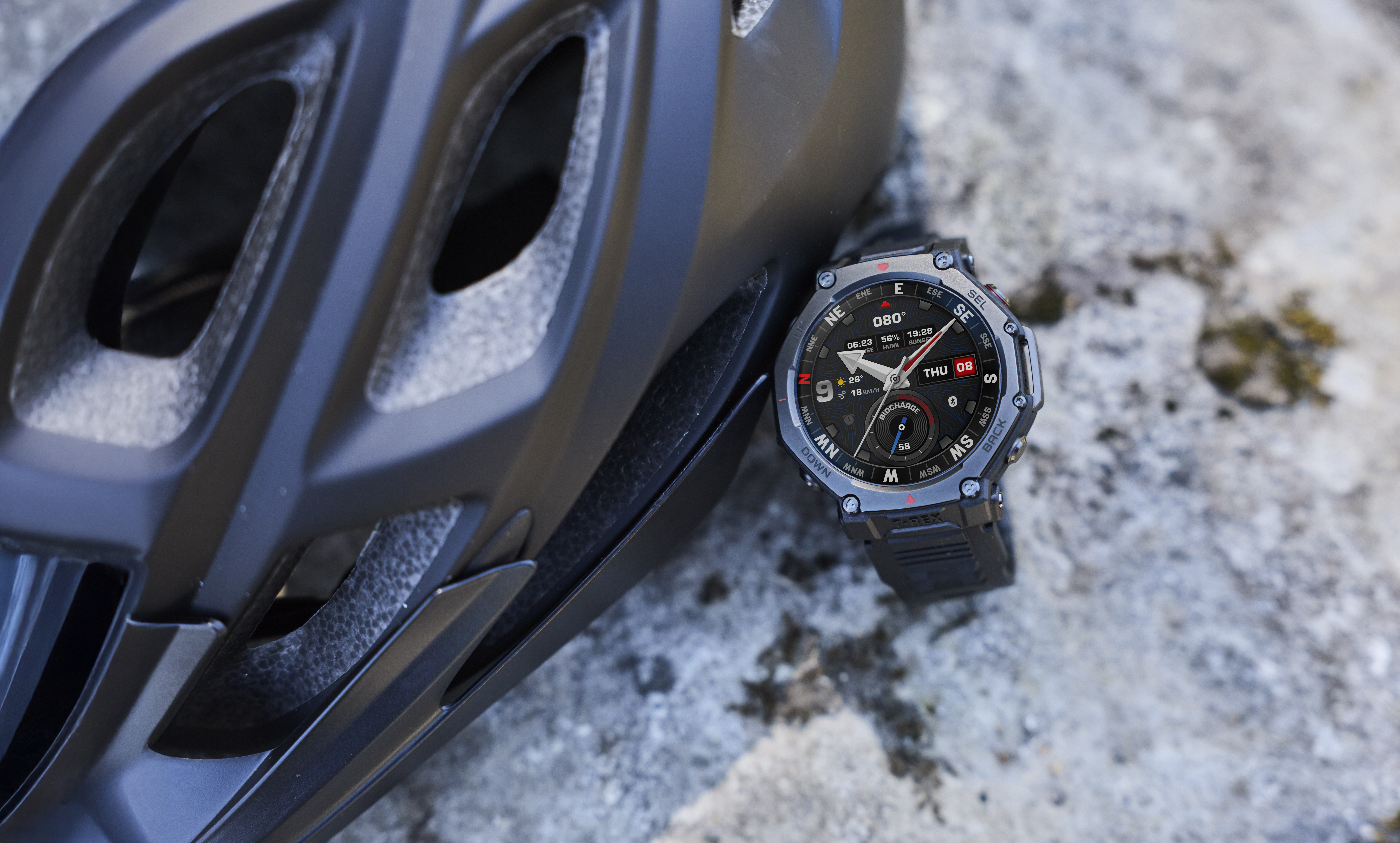 Czarny kask rowerowy i smartwatch leżą na skale.