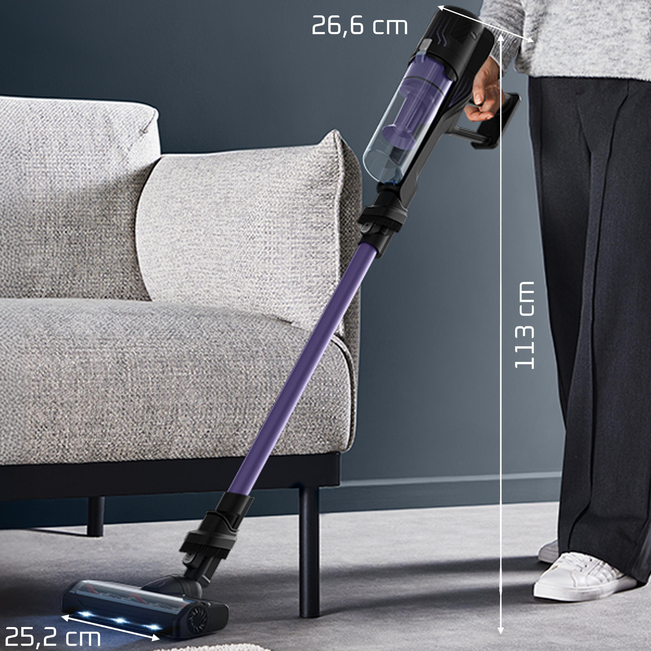Ein violetter Akku-Staubsauger wird neben einem grauen Sofa gehalten. Maße sind angegeben.