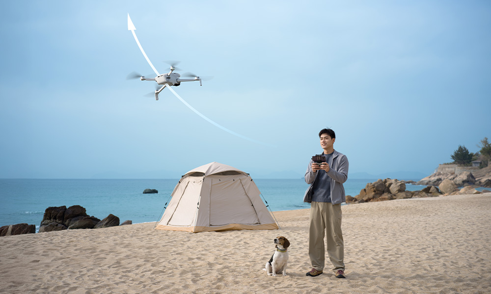 Mężczyzna z psem na plaży steruje dronem, namiot w tle.