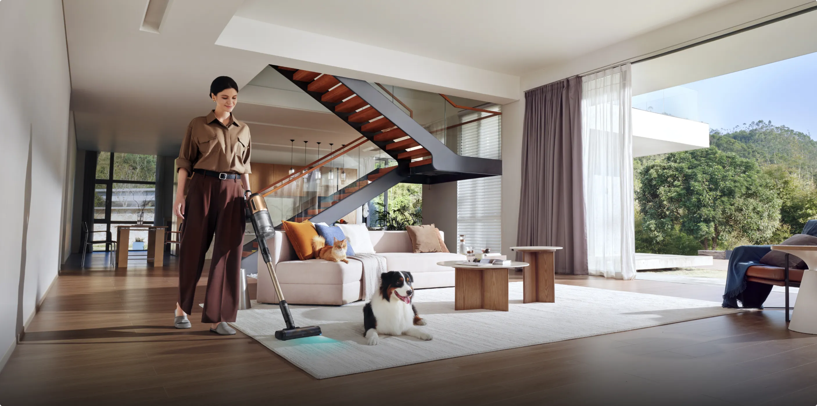 Eine Frau saugt einen Teppichboden in einem modernen Wohnzimmer mit einem Hund und einer Katze.