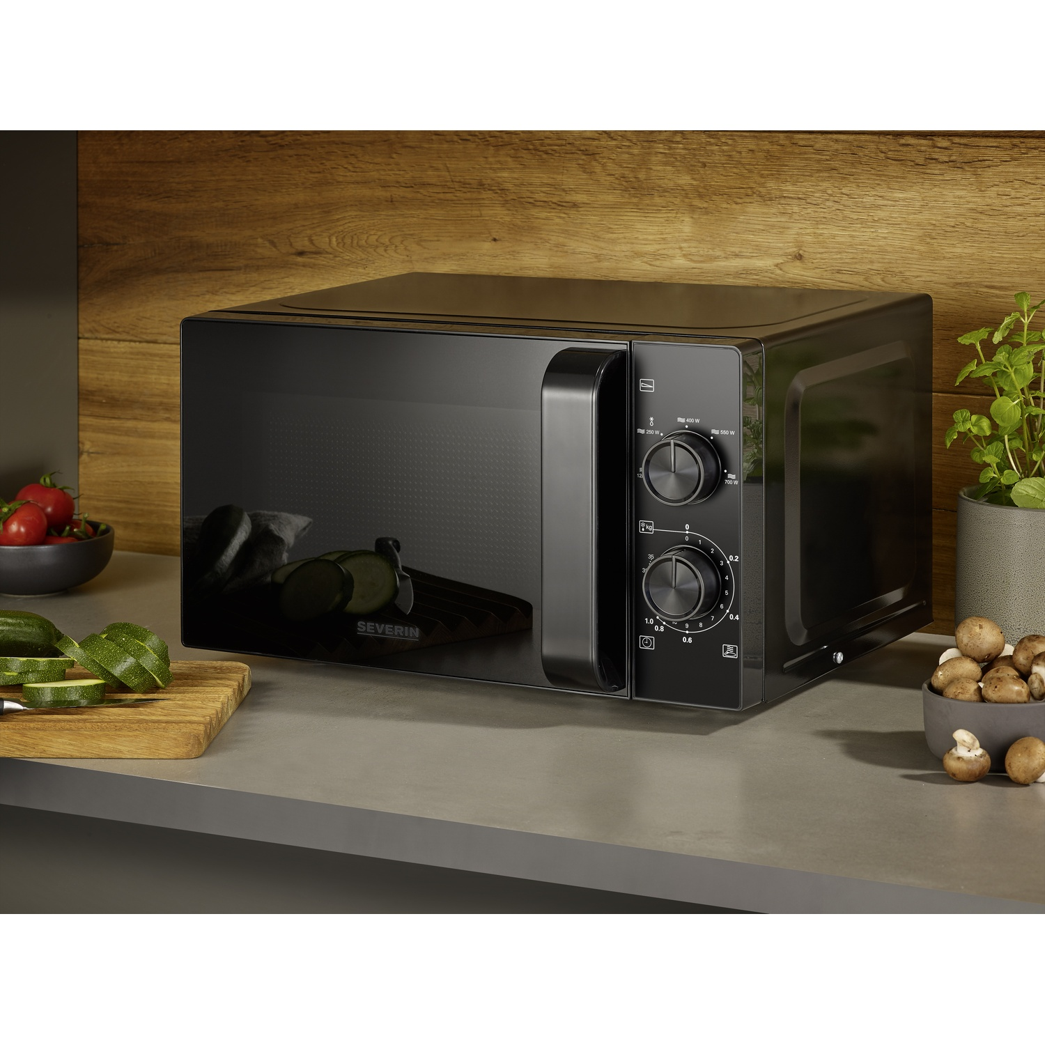 Black microwave with knobs and handle on a countertop with ingredients.