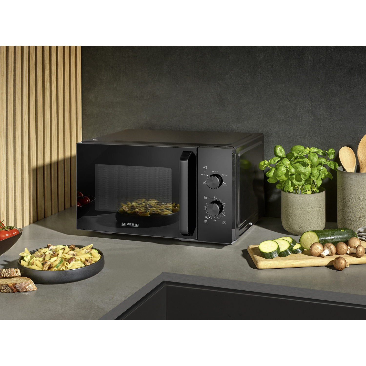Black microwave with pasta, vegetables, and mushrooms on a countertop.