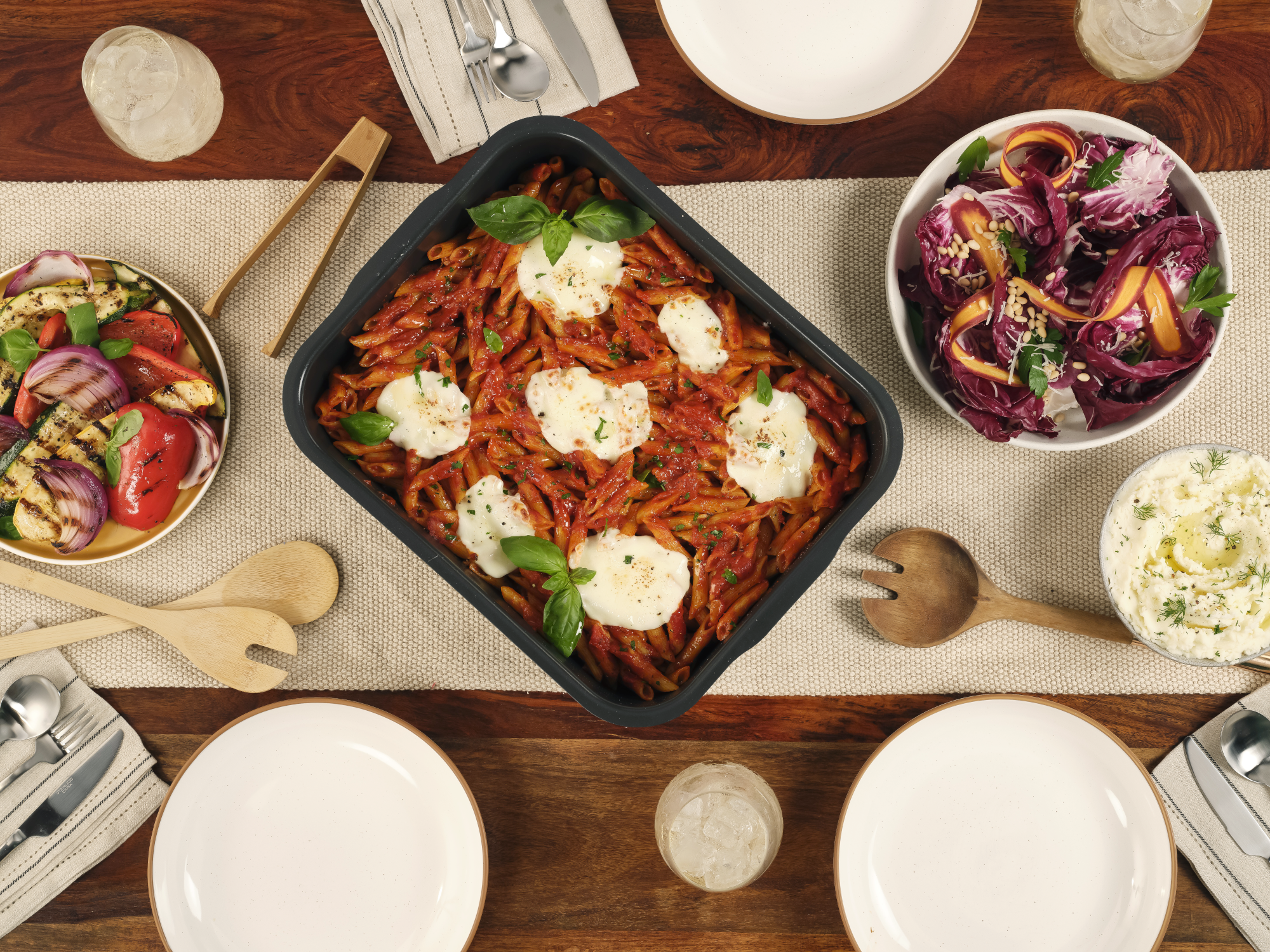 Az asztalon penne tészta, grillezett zöldségek, saláta, krumplipüré és italok vannak.