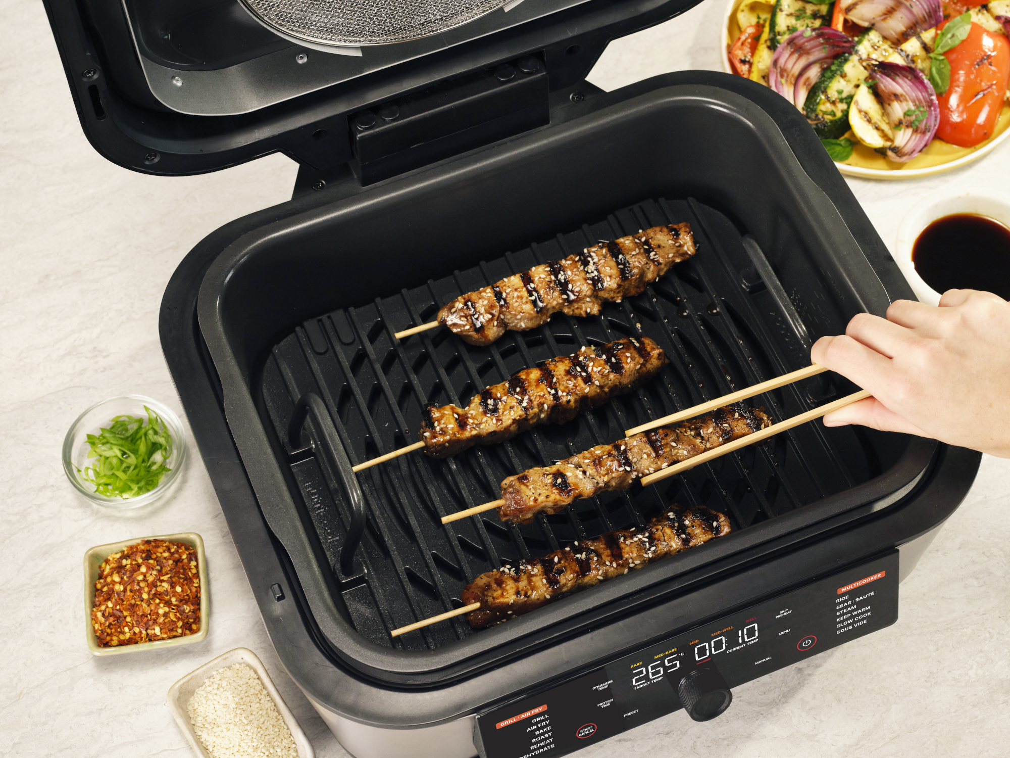 Szezám magos húsnyársakat grilleznek. Mellettük fűszerek.