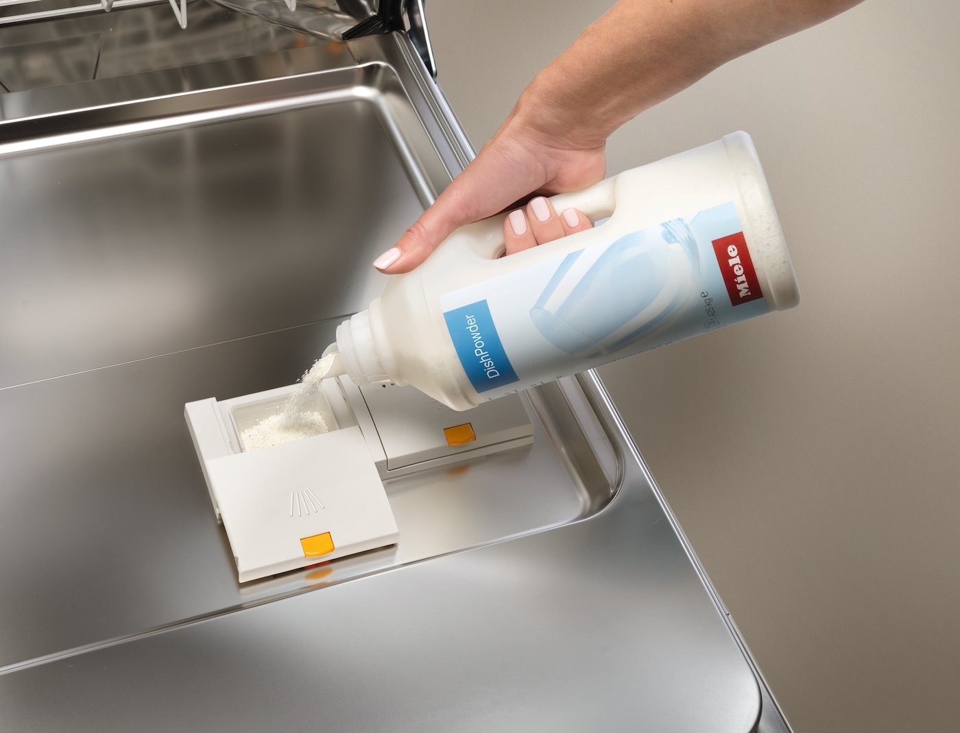 Eine Hand schüttet Spülpulver aus einer weißen Flasche in einen Spülmittelbehälter.