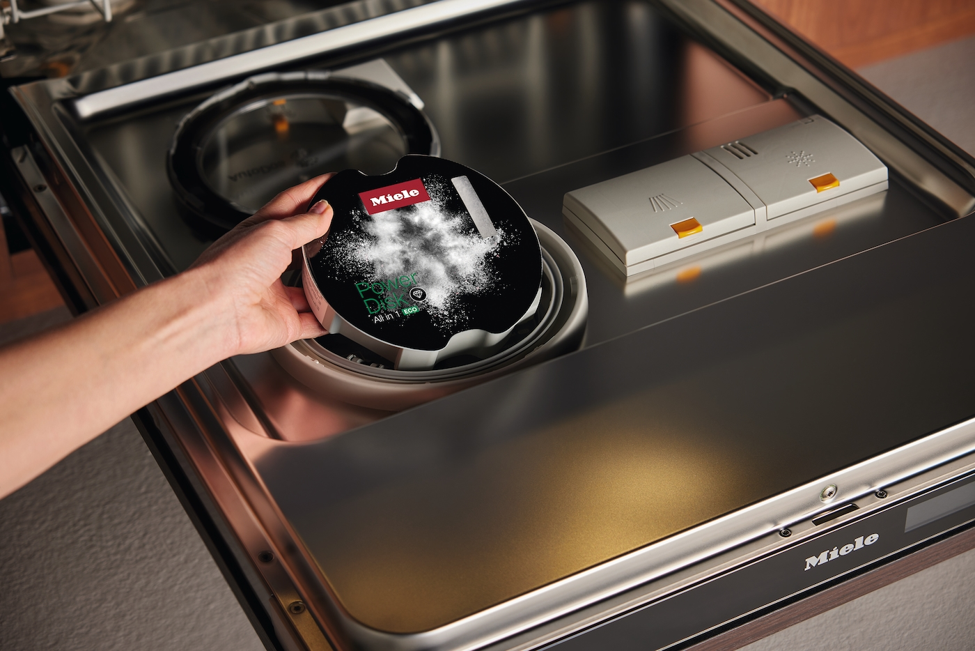 Eine Hand legt eine Miele PowerDisk-Spülmaschinentablette in eine offene Spülmaschine.