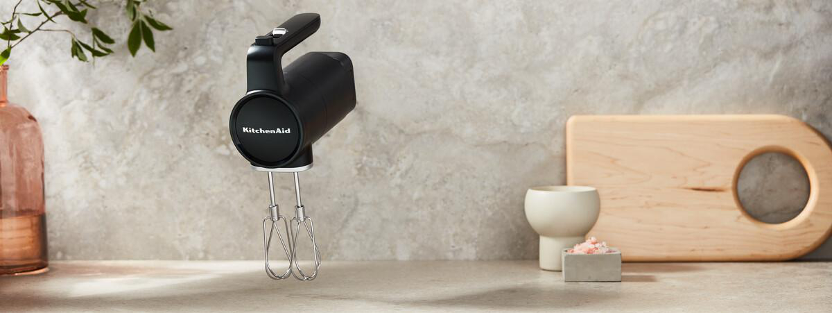 Schwarzer KitchenAid Handmixer mit Schneebesen auf einer Marmoroberfläche.