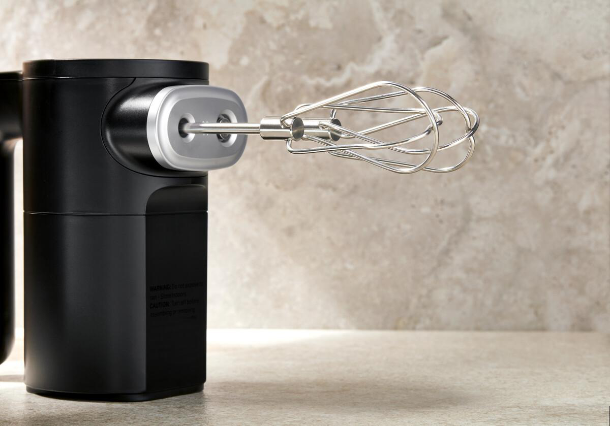 Ein schwarzer Handmixer mit silbernem Kopf und einem Schneebesen-Aufsatz auf Stein.