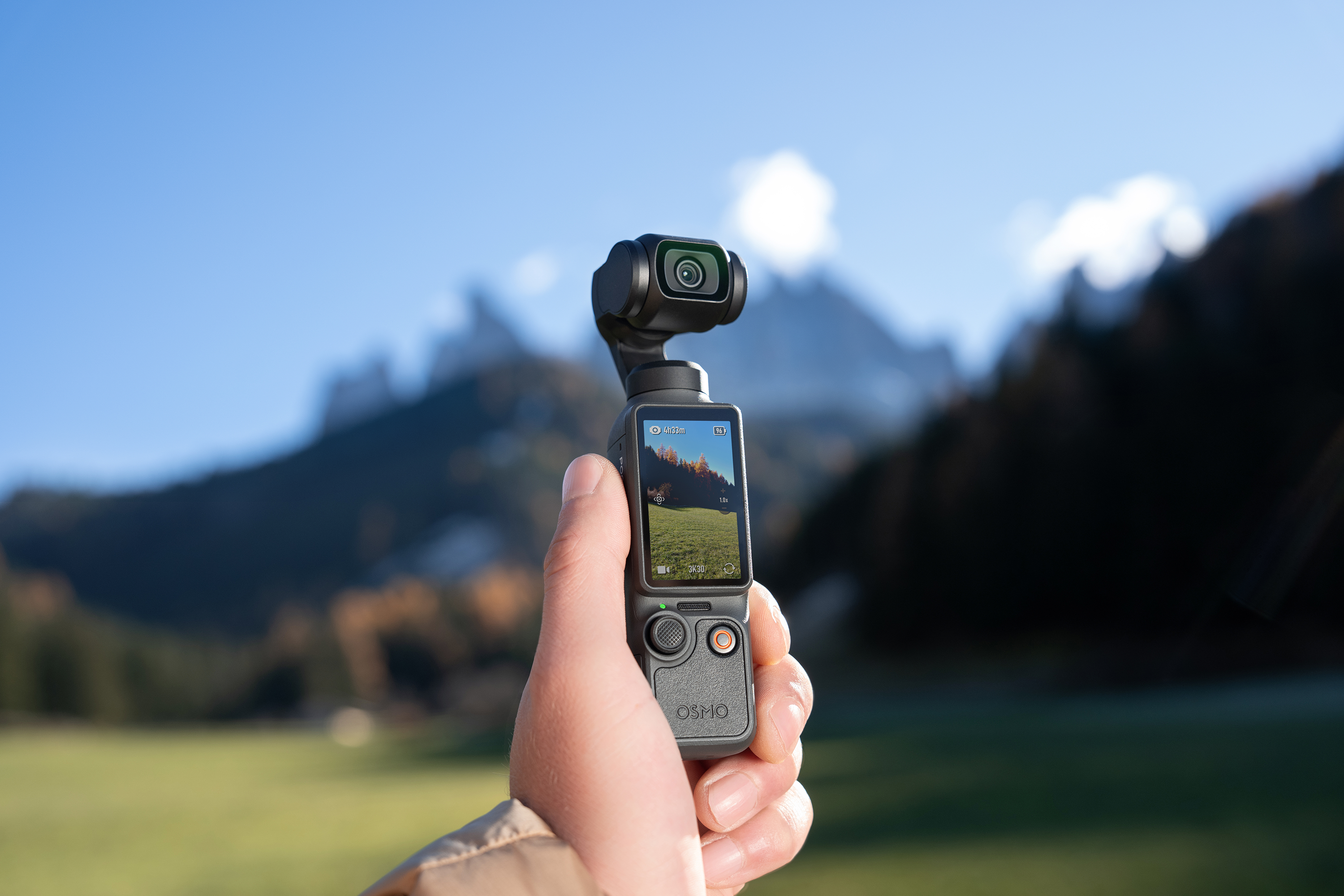 Kézből tartott gimbal kamera hegyvidék előtt, kék égbolttal.