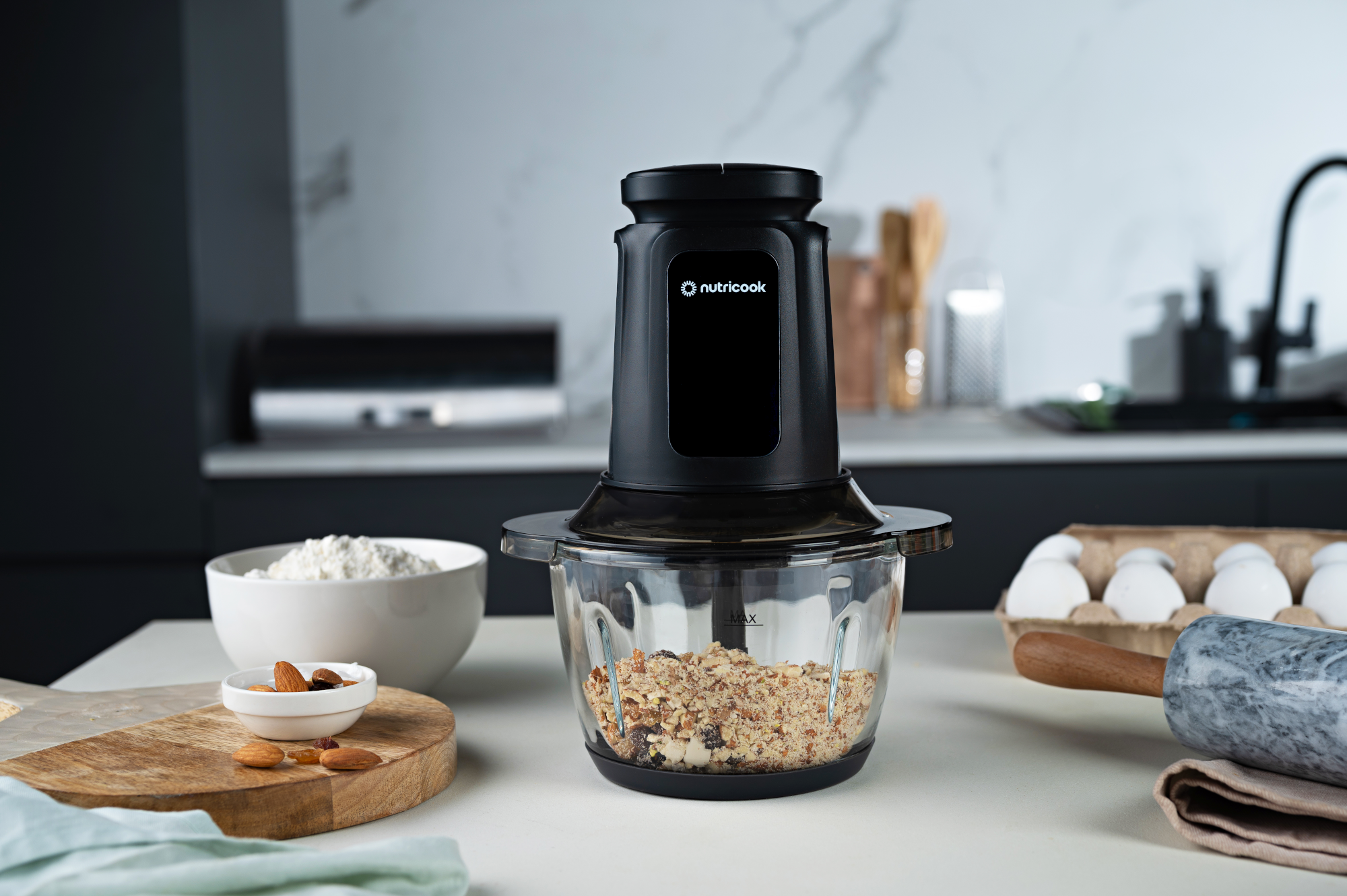 Egy fekete Nutricook konyhai robotgép dióval és aszalt gyümölccsel az asztallapon.