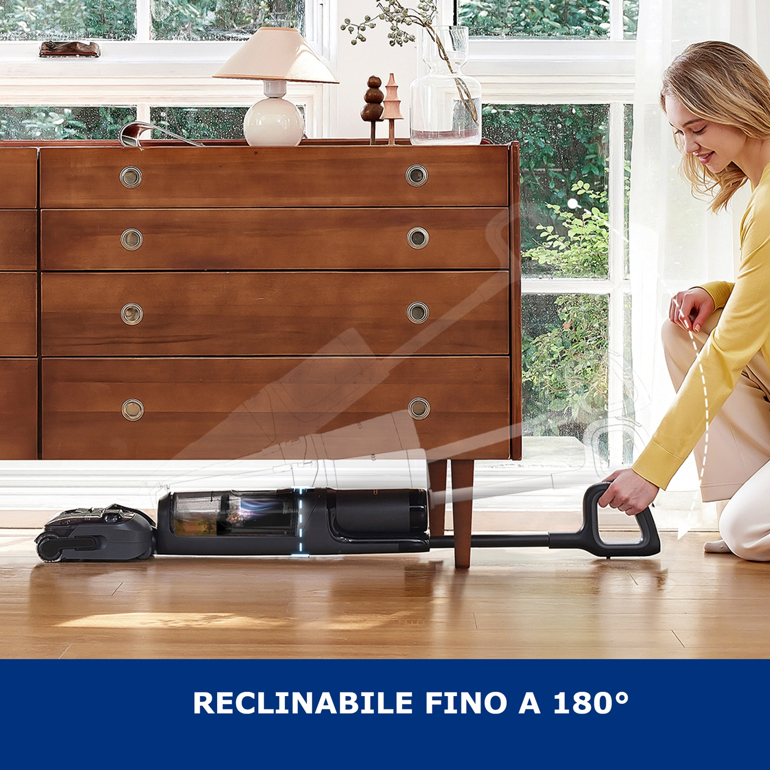 Una donna usa un aspirapolvere nero sotto una cassettiera di legno.