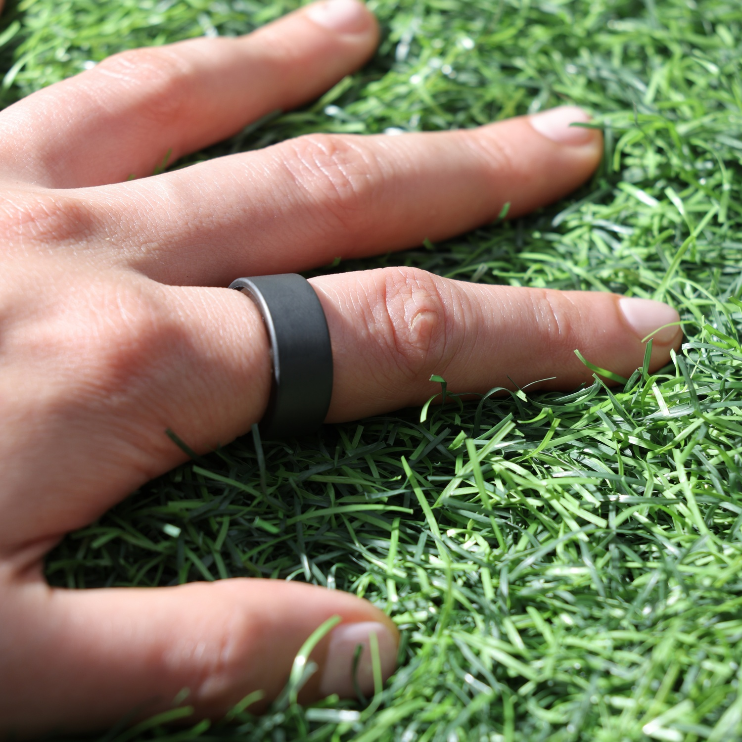 Una mano con un anello nero poggia sull'erba sintetica verde.