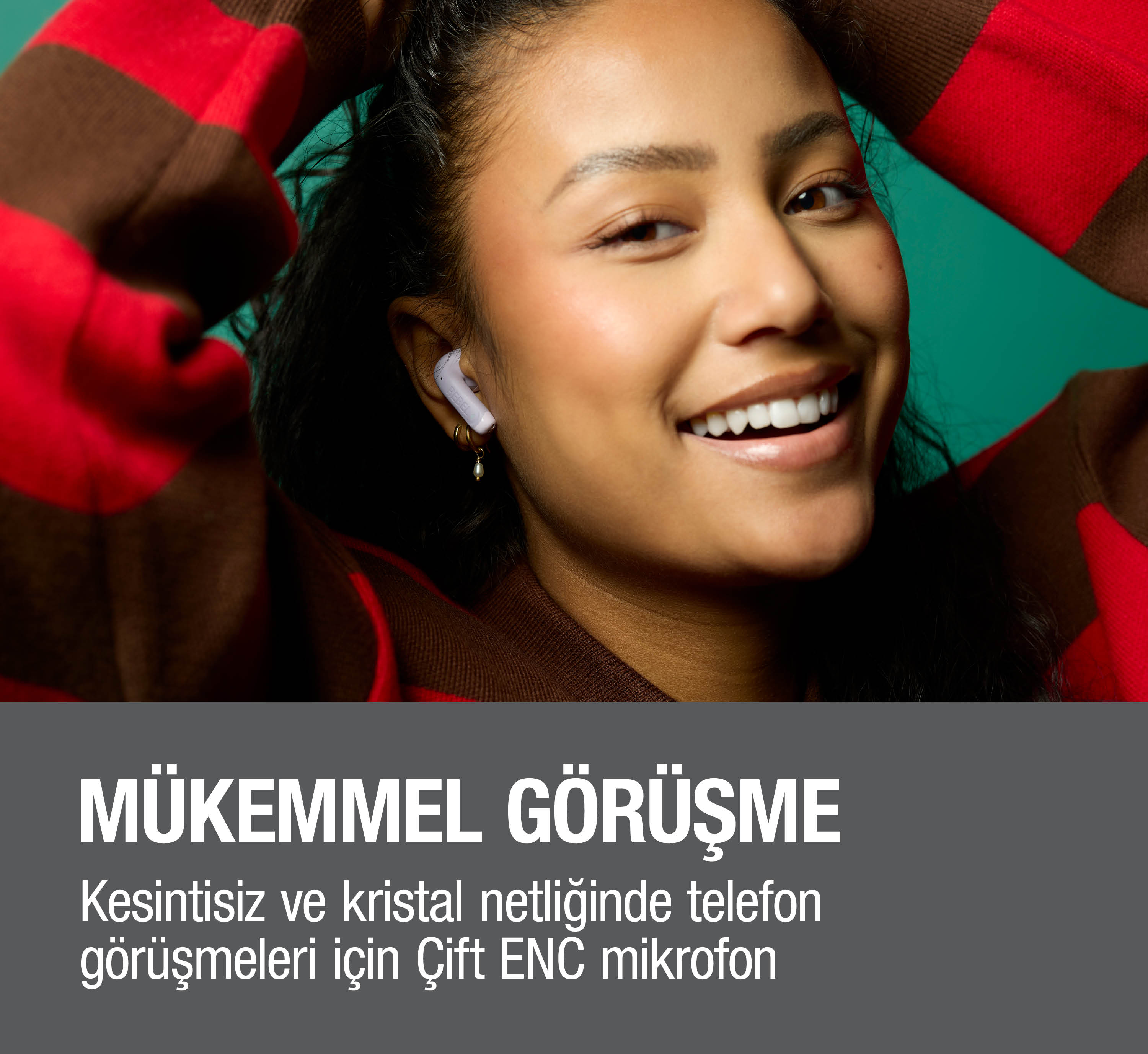 Kulaklıklı kadın, çizgili kazakla turkuaz fon önünde gülümsüyor.