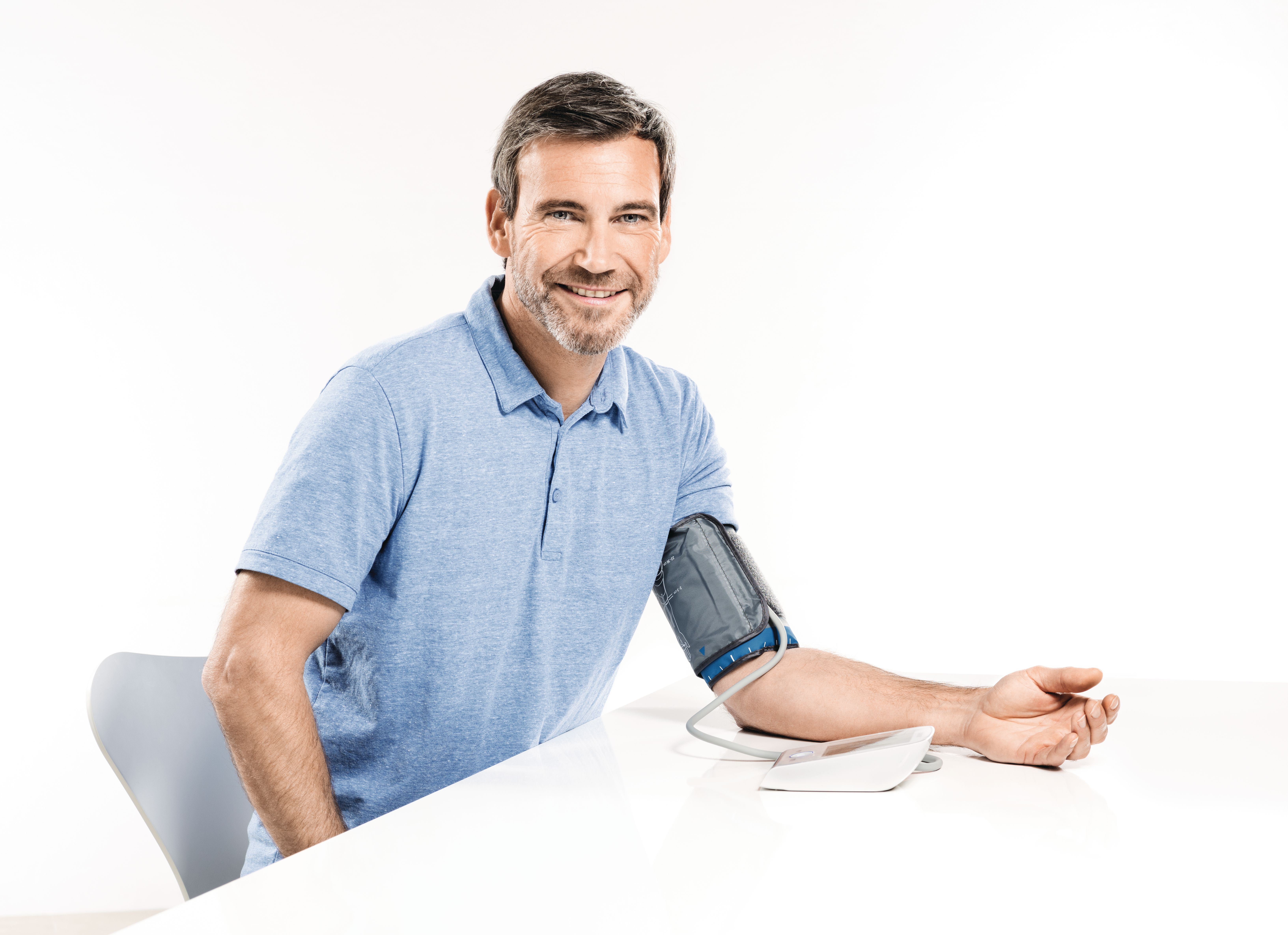 Ein Mann mit blauem Poloshirt misst seinen Blutdruck mit einem Gerät.
