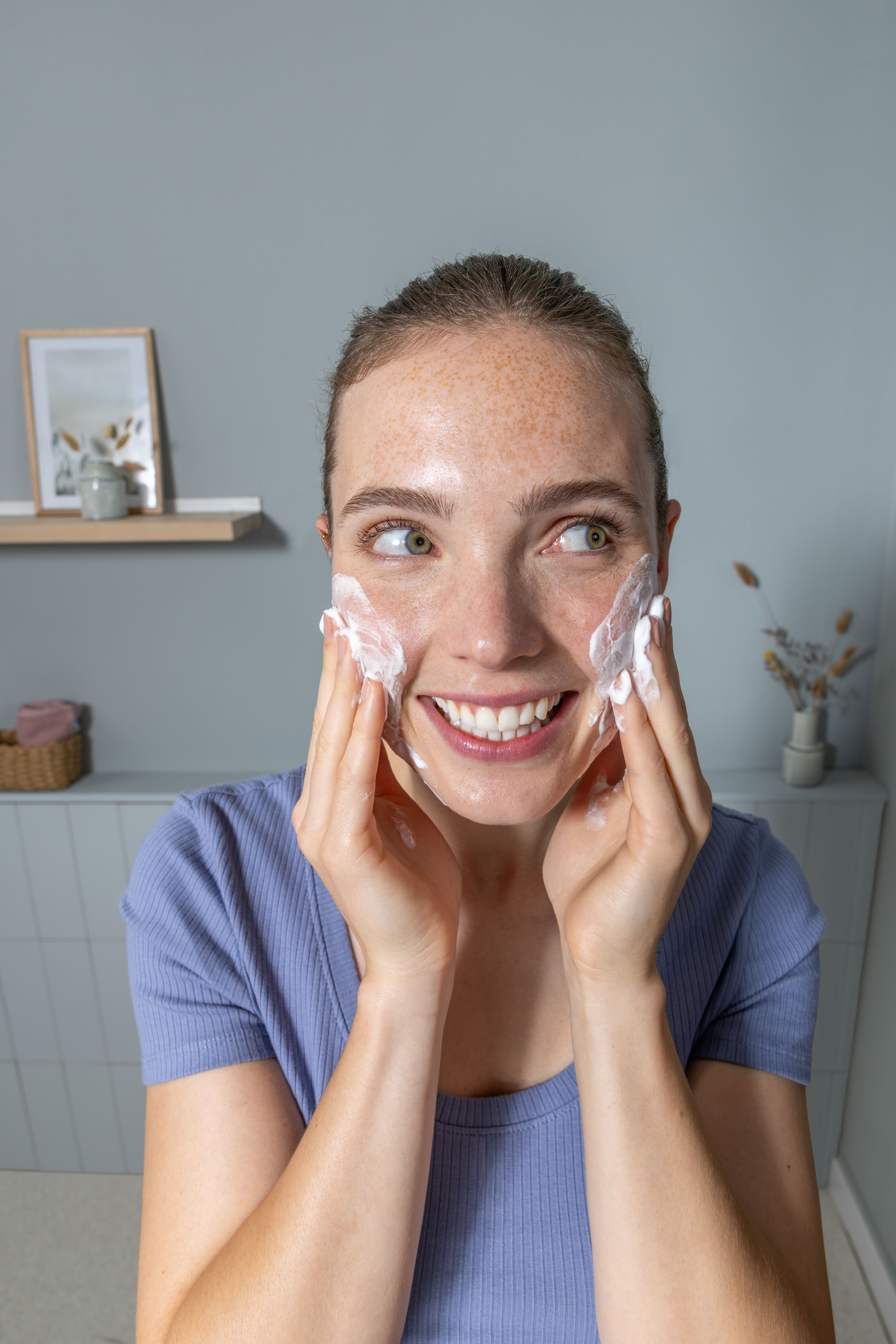 Eine Frau mit Sommersprossen wäscht ihr Gesicht mit Schaum in einem Badezimmer.
