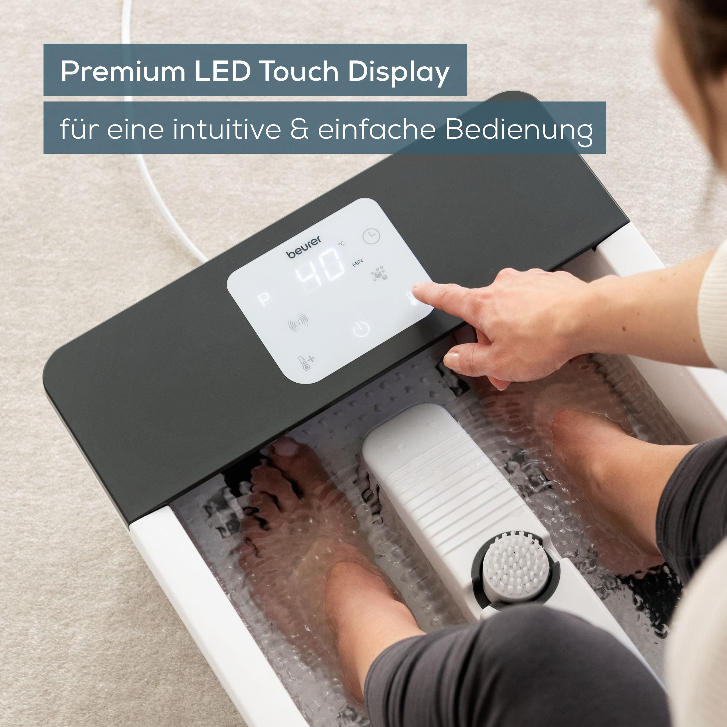 Füße in einem Beurer Fußsprudler mit 40°C, Person bedient das Display.