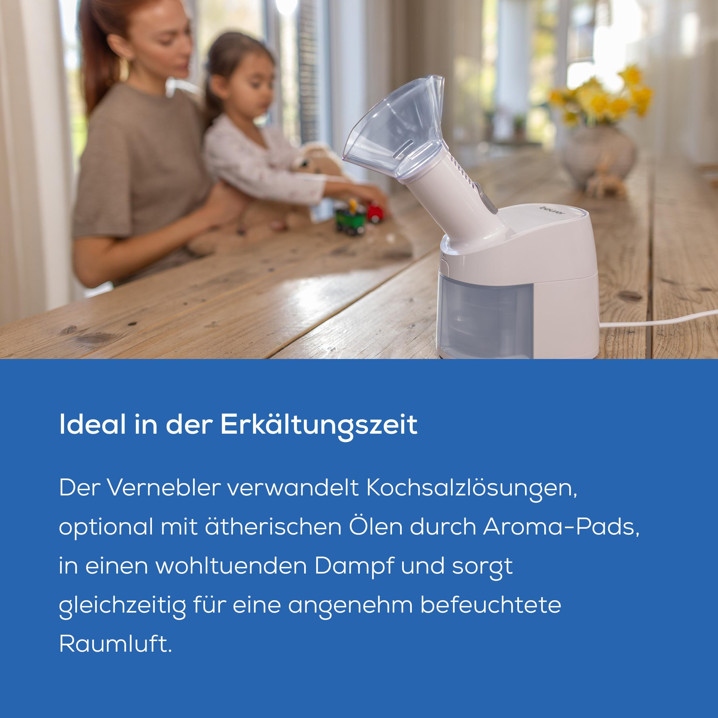 Eine Frau und ein Kind sitzen an einem Holztisch, ein Vernebler steht vorn.