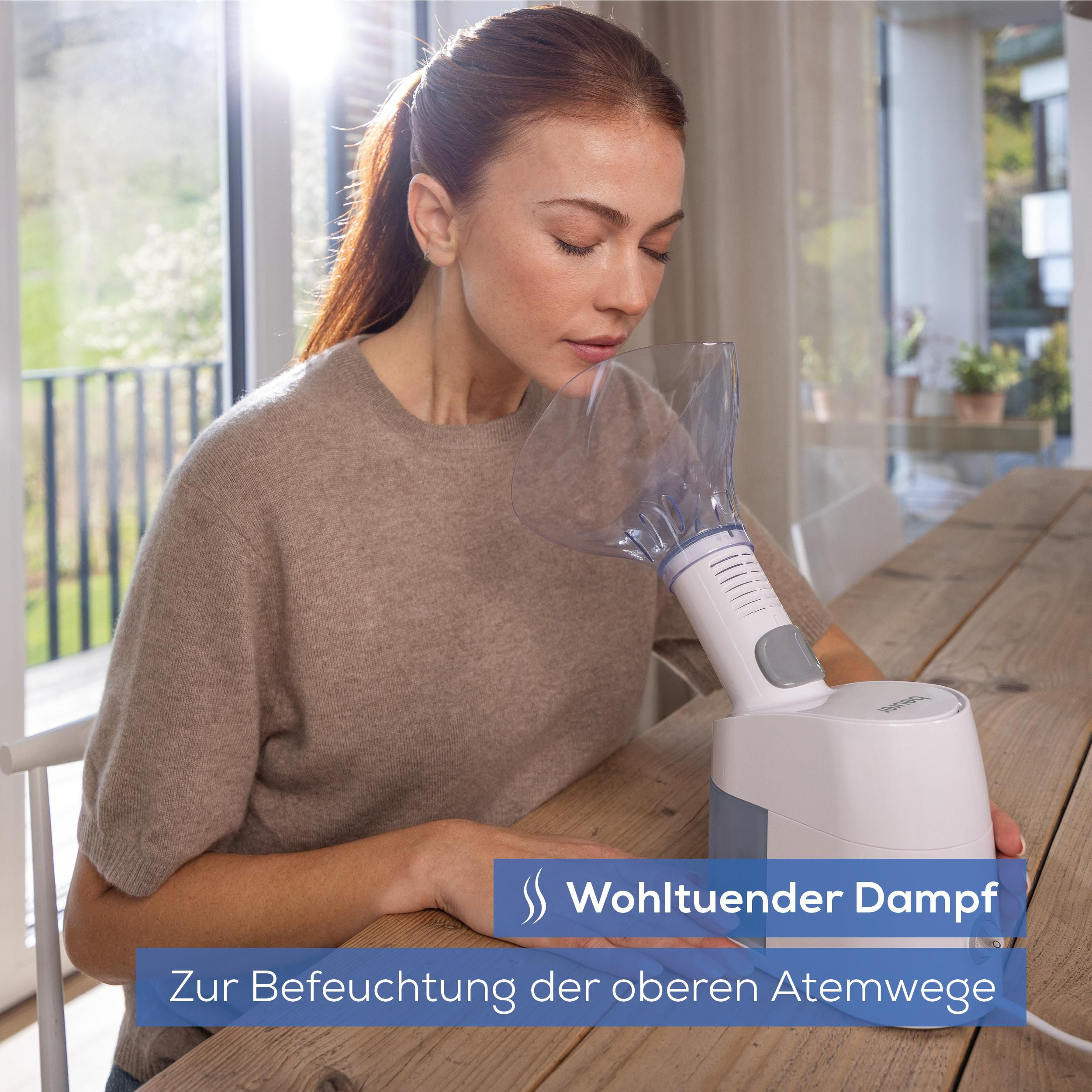 Frau inhaliert Dampf aus einem weißen Inhalator auf einem Holztisch.