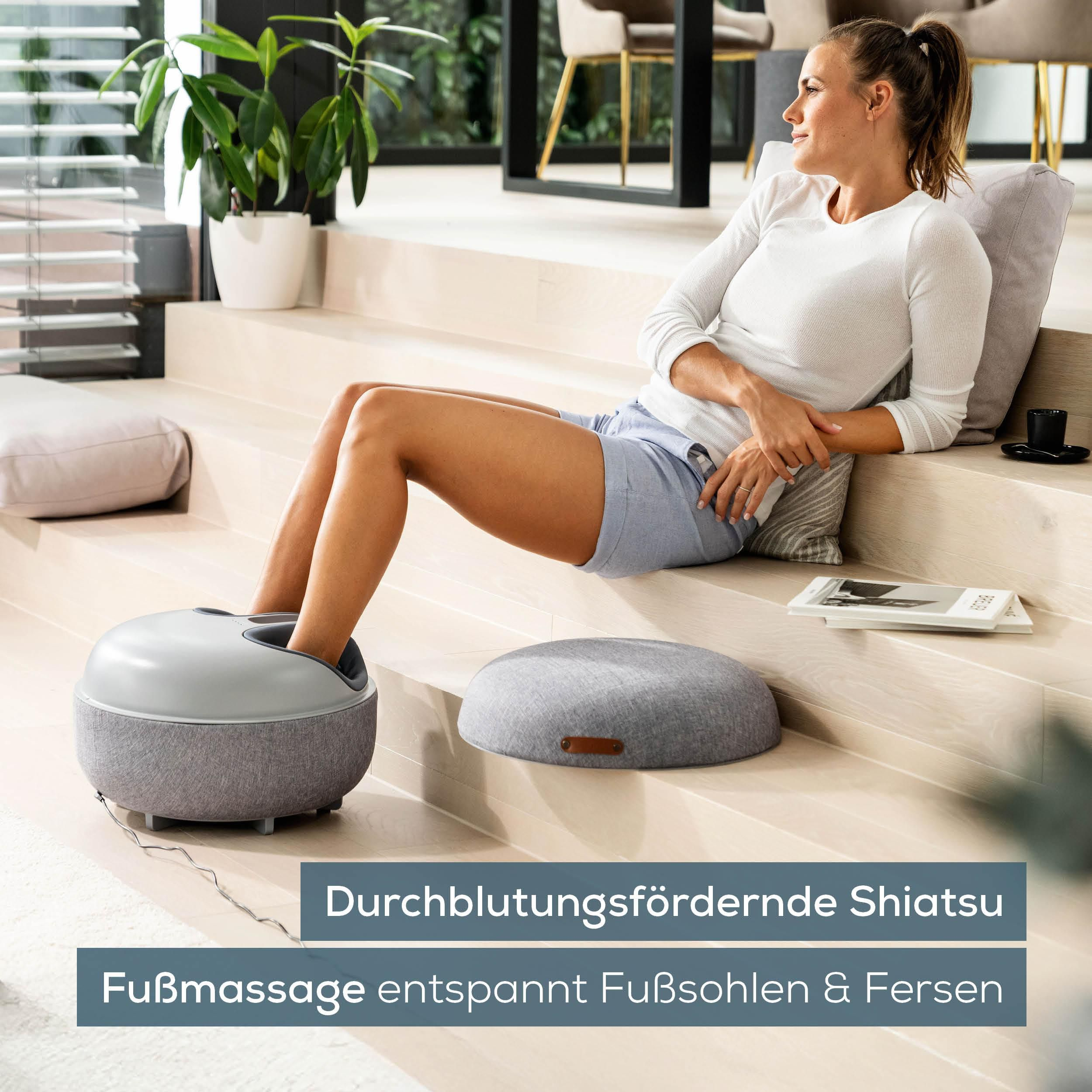 Frau sitzt auf Treppen, Füße in Massagegerät. Grauer Hocker daneben.