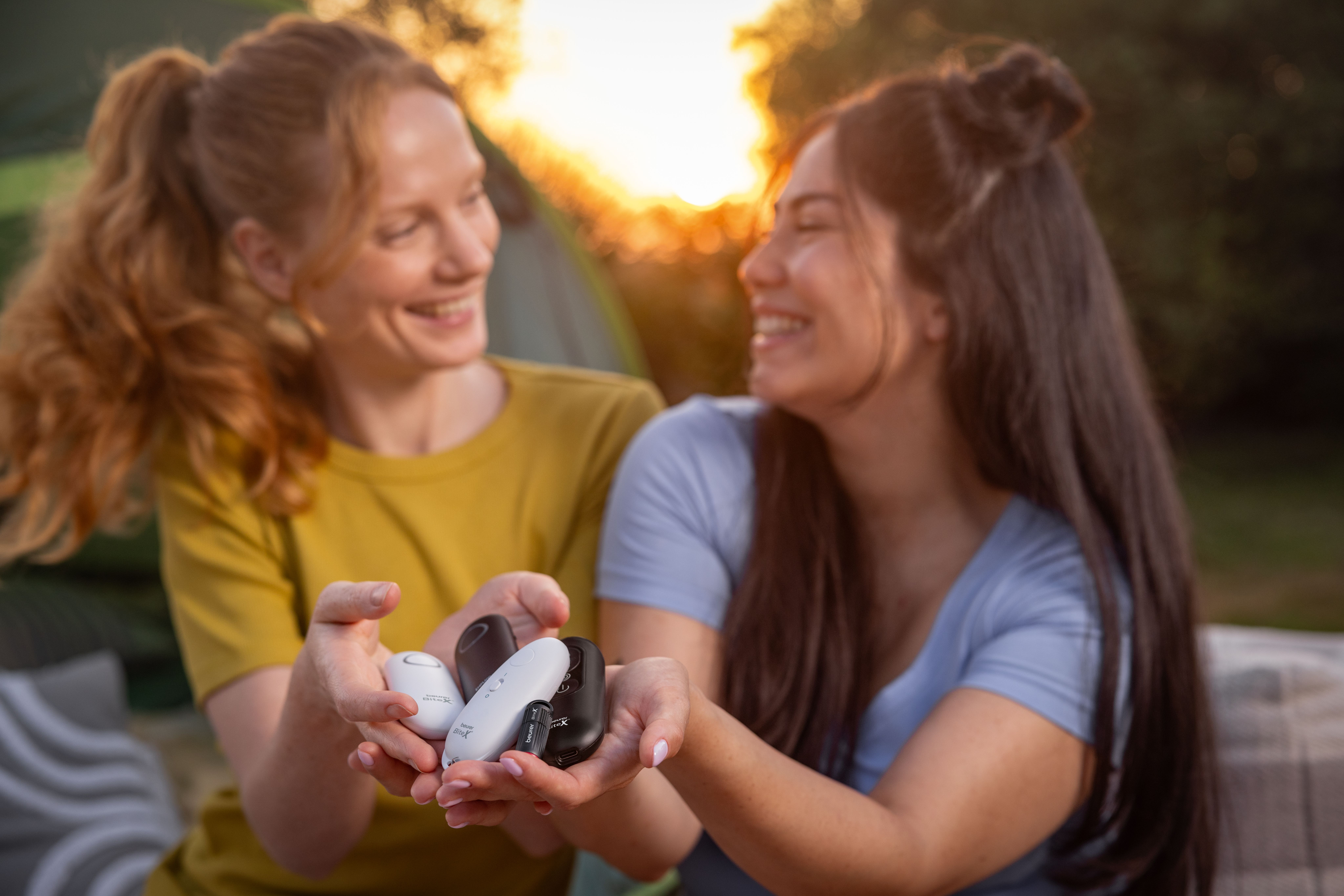 Zwei lächelnde Frauen halten Insektenstichheiler im Freien bei Sonnenuntergang.
