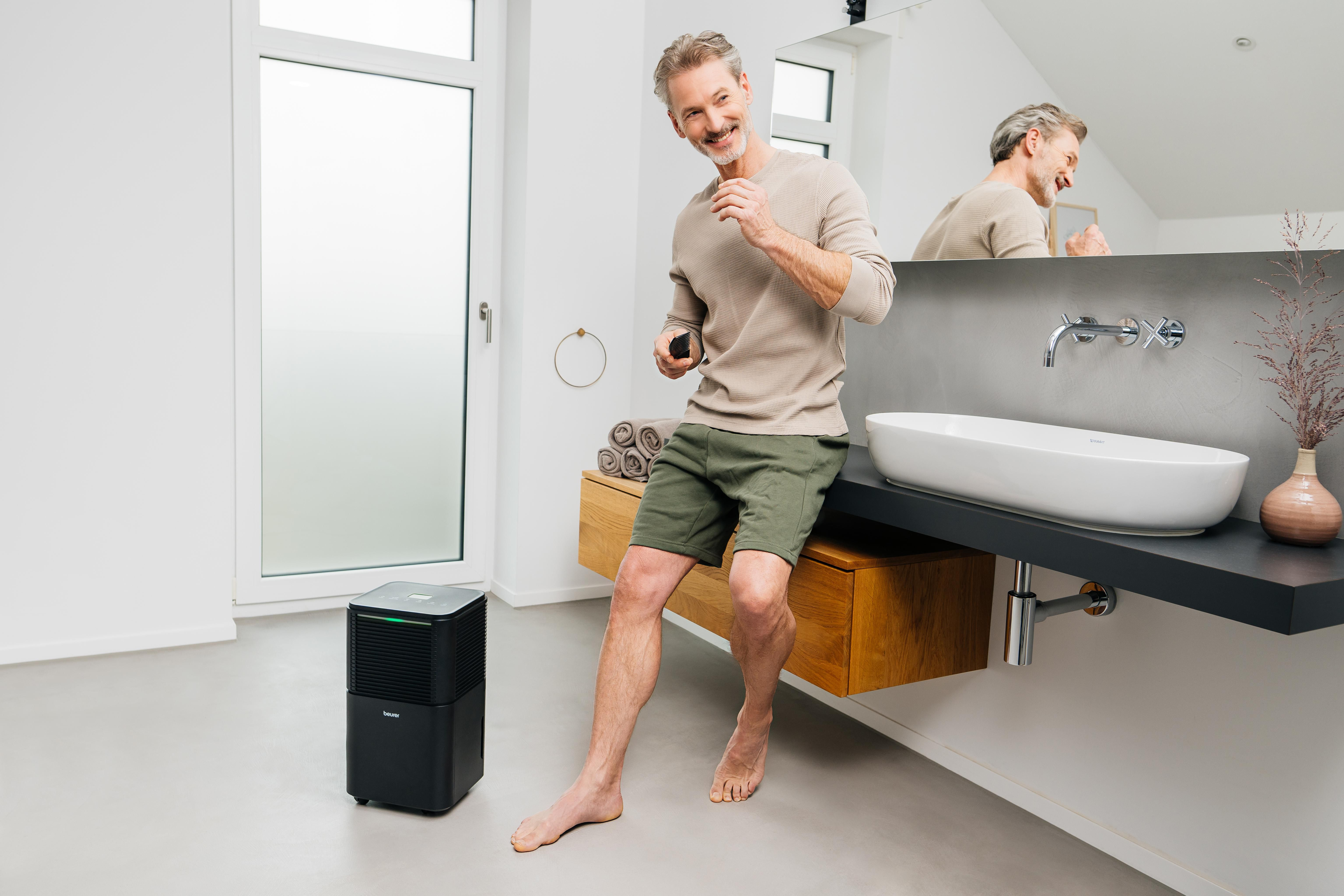 Mann im Badezimmer mit Haarschneider neben Luftentfeuchter.