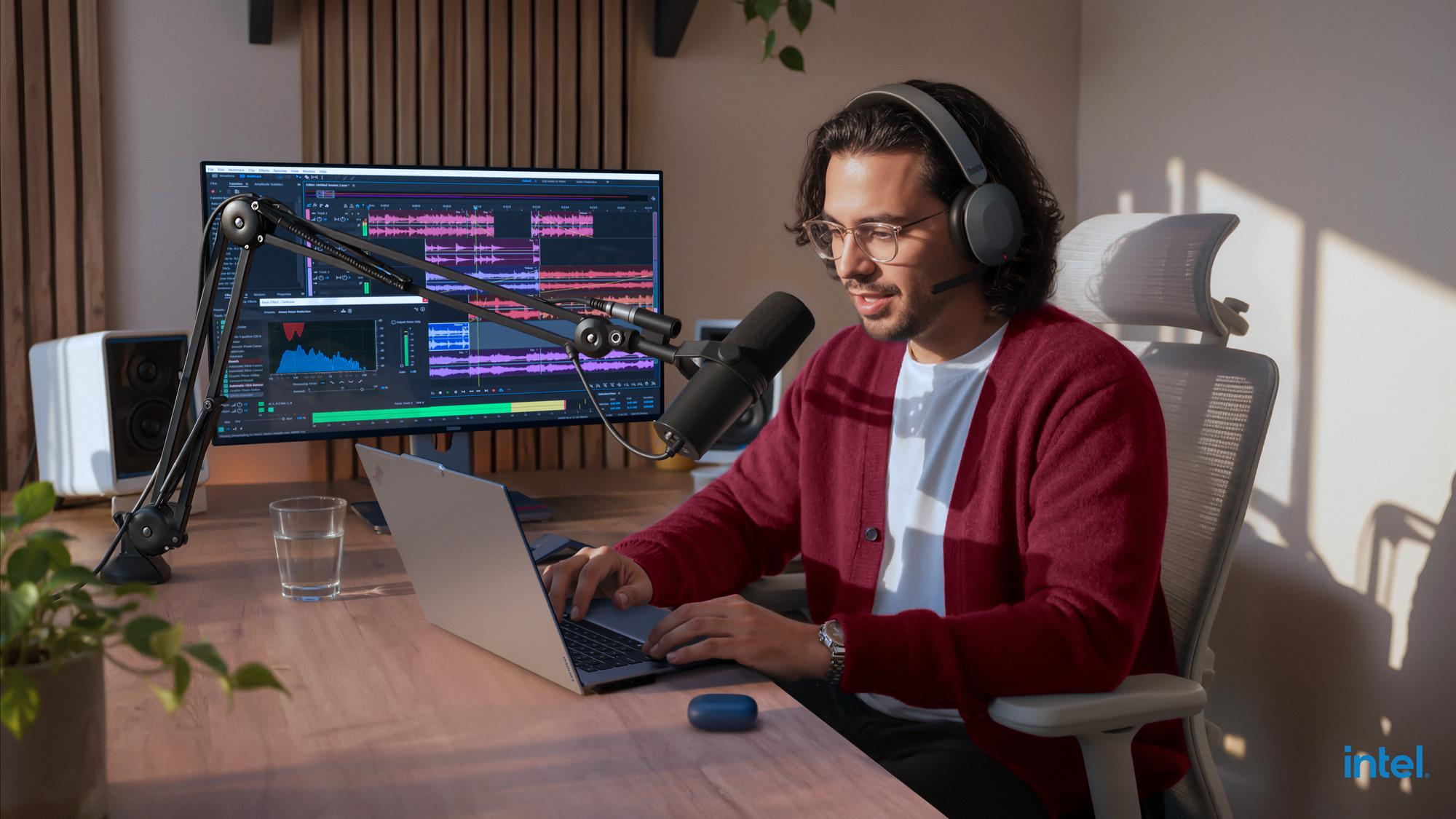 Ein Mann mit Kopfhörern arbeitet an einem Laptop vor einem Monitor mit Audio-Software.