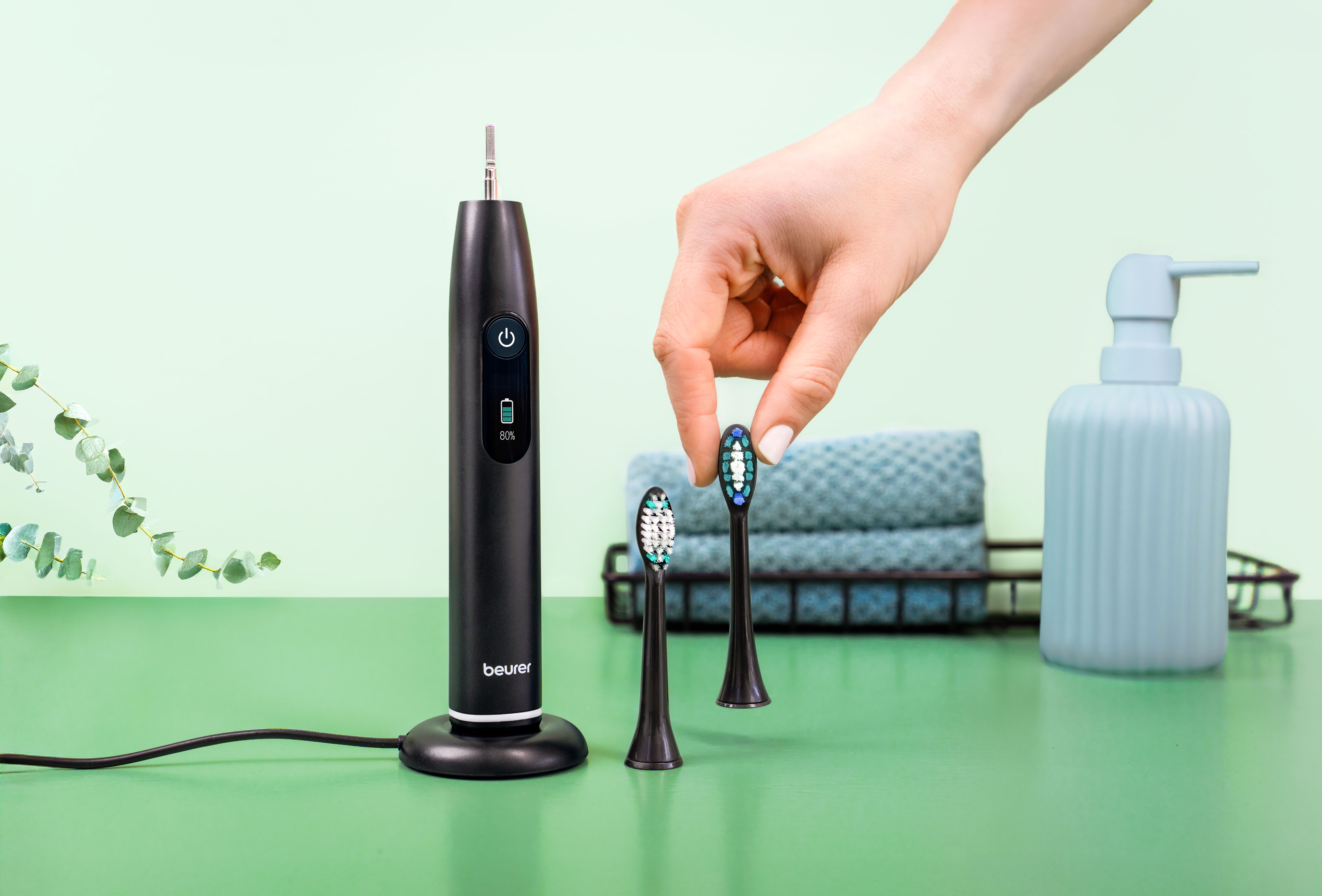 Schwarze elektrische Zahnbürste mit zwei Aufsätzen, Seifenspender und Handtuch.