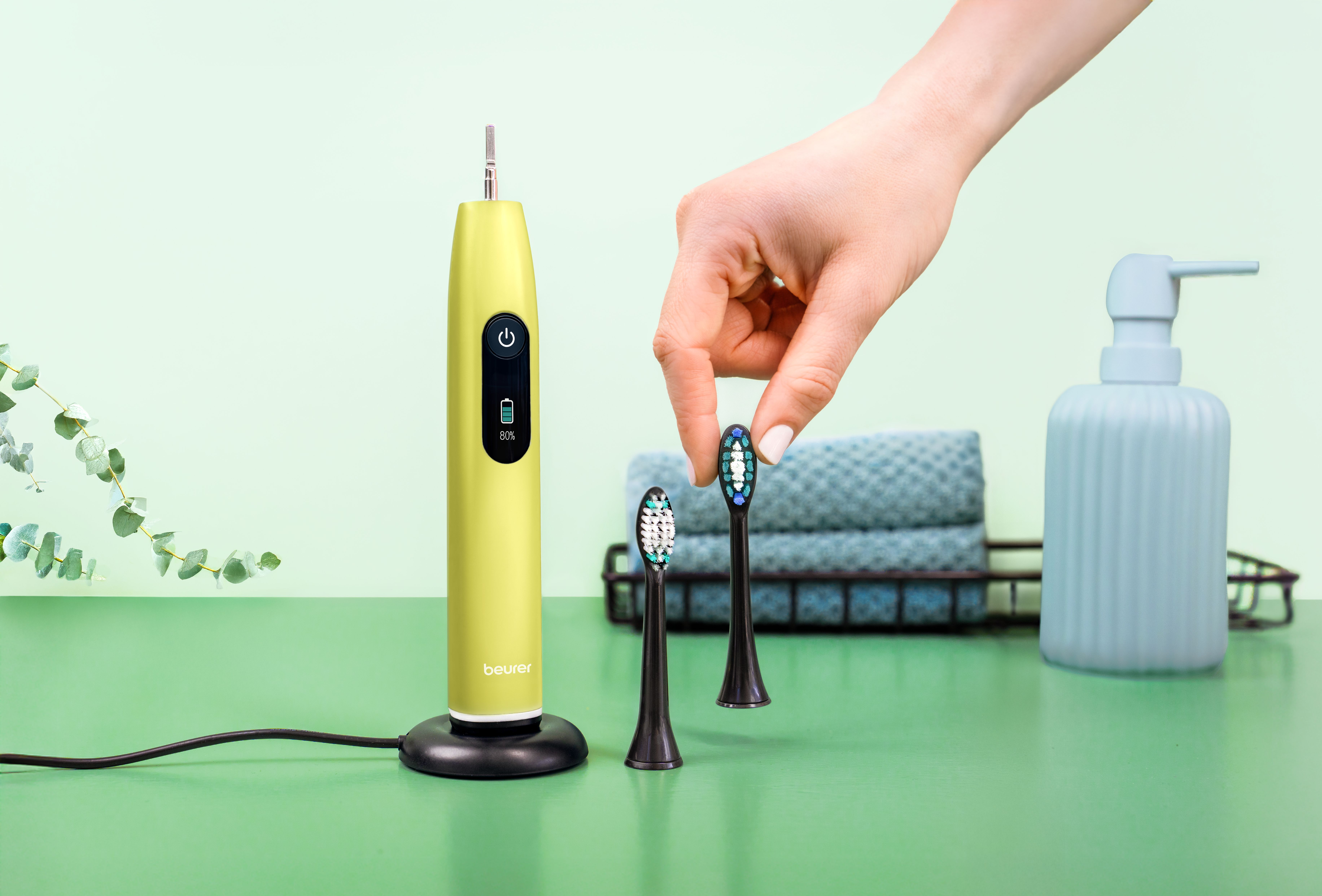 Ein gelbes elektrisches Zahnbürsten-Set mit zwei Bürstenköpfen auf grünem Untergrund.